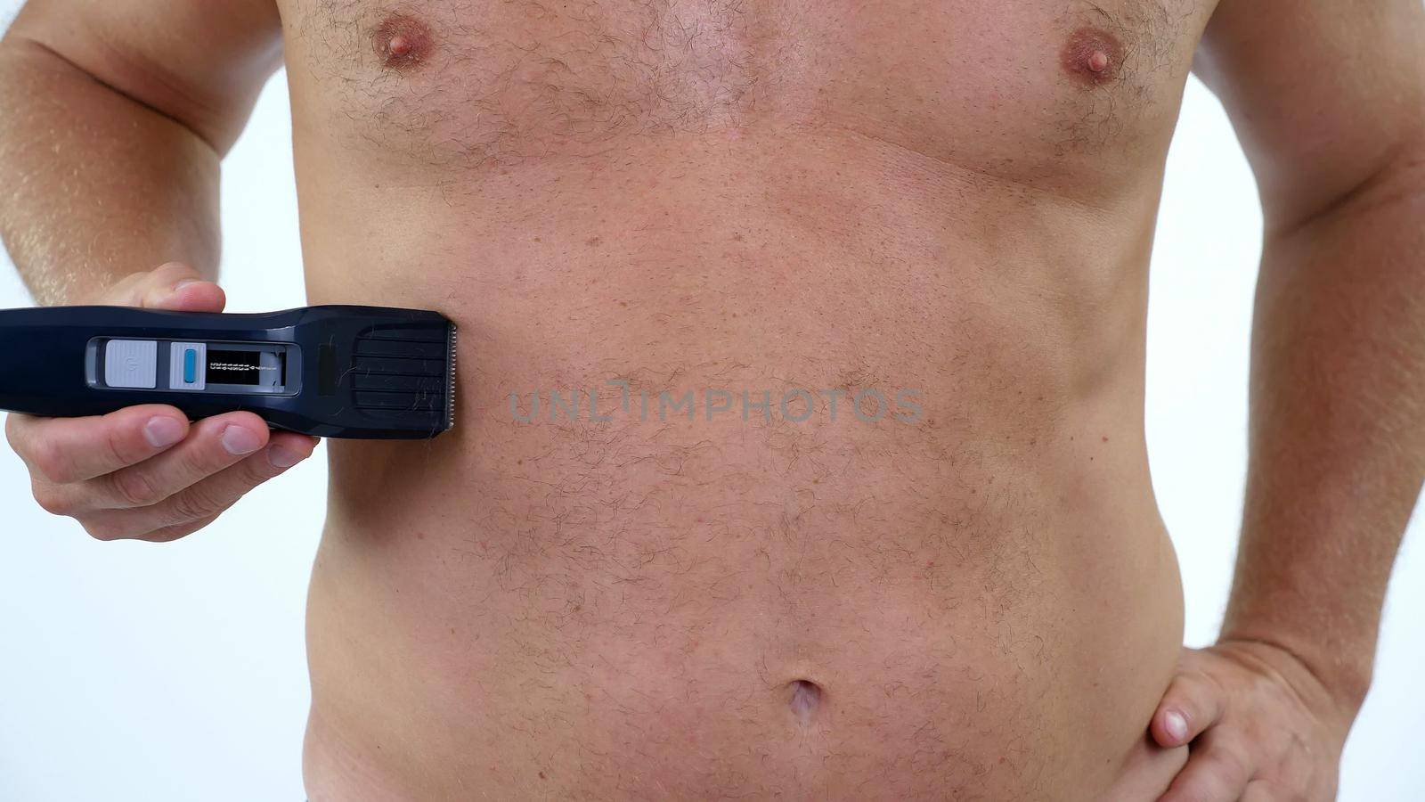 Close-up of a very hairy Man haircut body hair on his, male chest by himself with a clipper, electric razor, trimer. isolated on white background. Naked man shaves his chest. High quality photo