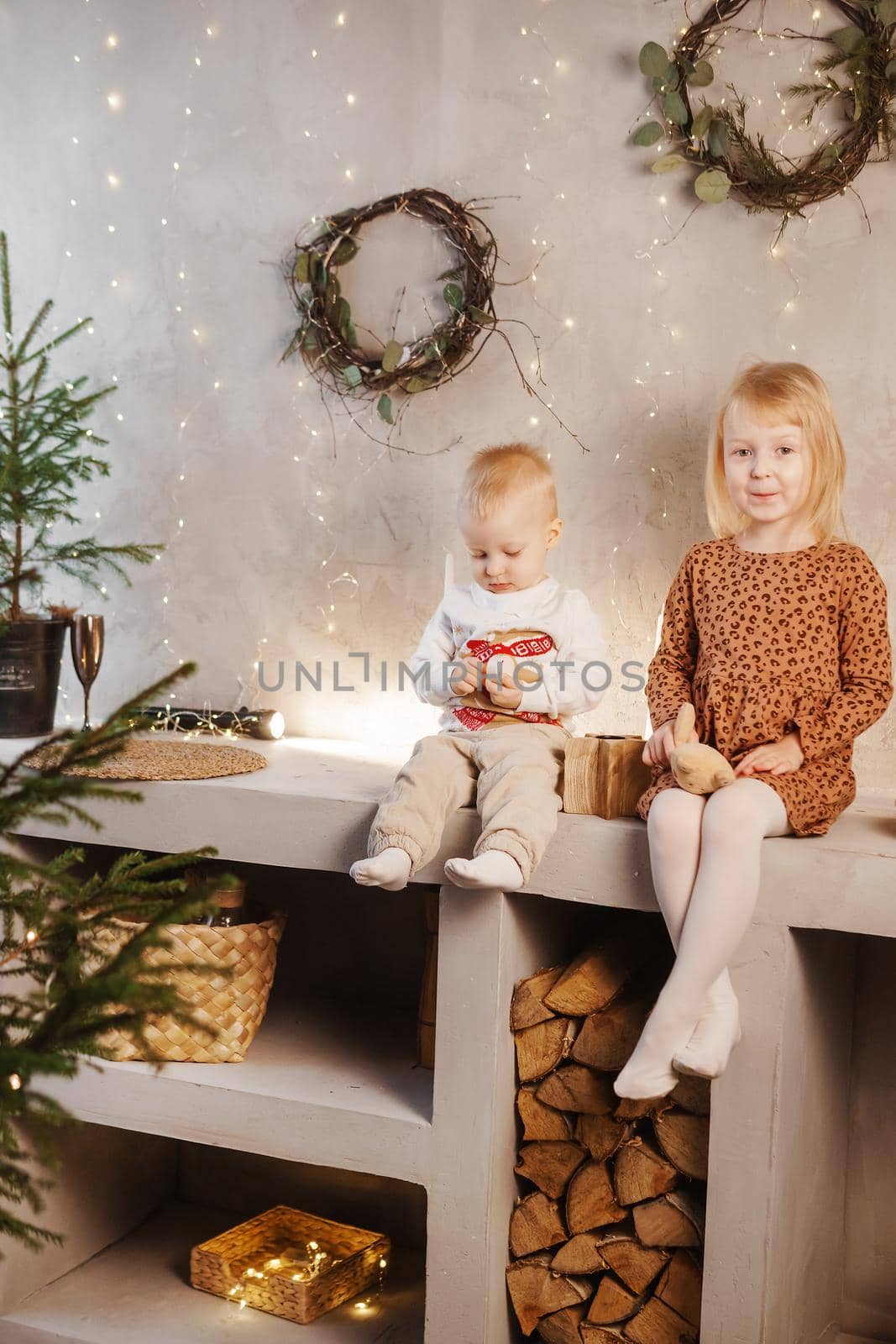 Little brother and sister play on Christmas eve in a beautiful house decorated for the New Year holidays. Children are playing with a Christmas gift. Scandinavian-style interior with live fir trees and a wooden staircase.