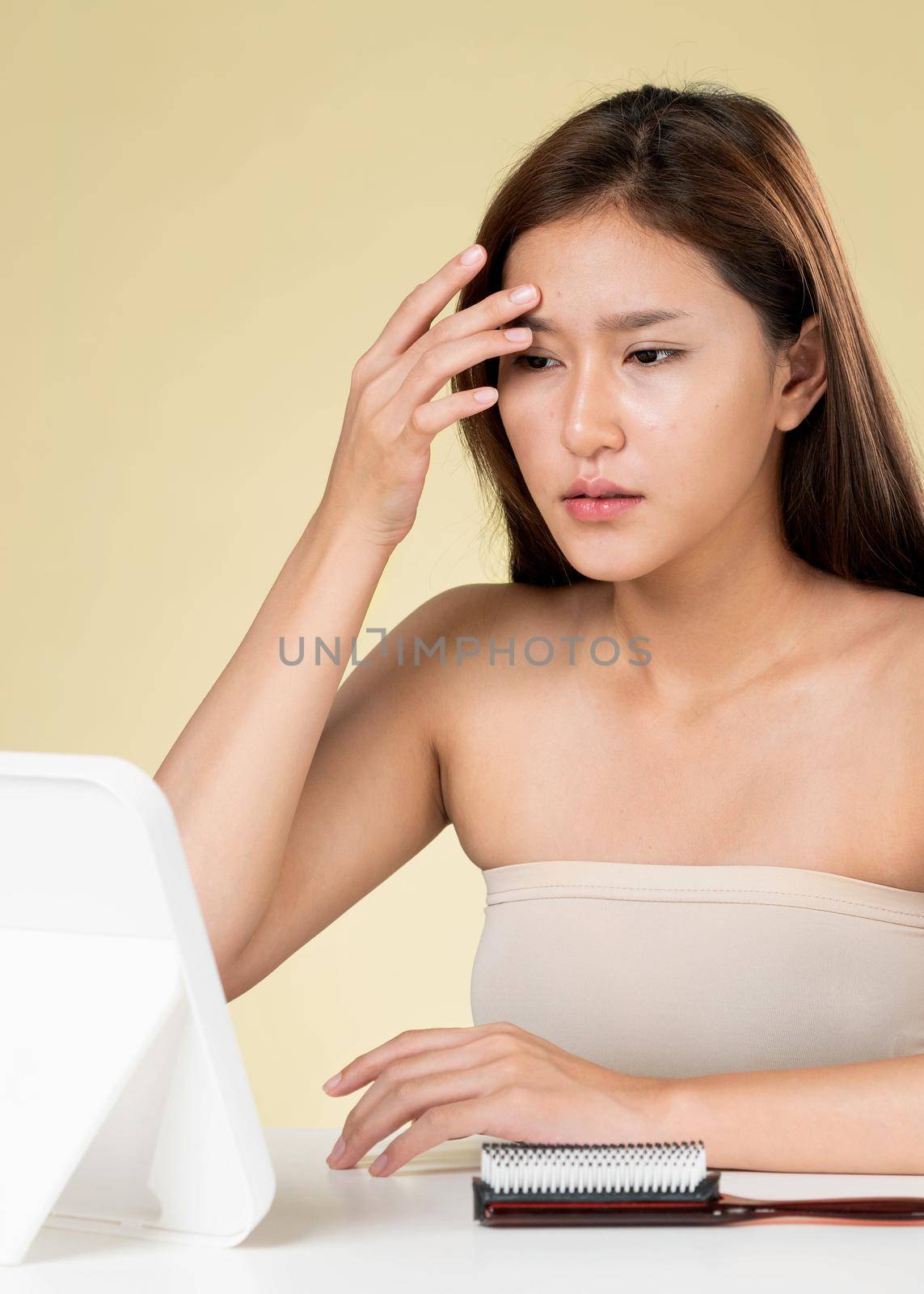 Portrait of young ardent asian woman looking in the mirror worry about pimple on her face. Beauty care for skin problem, acne treatment concept.