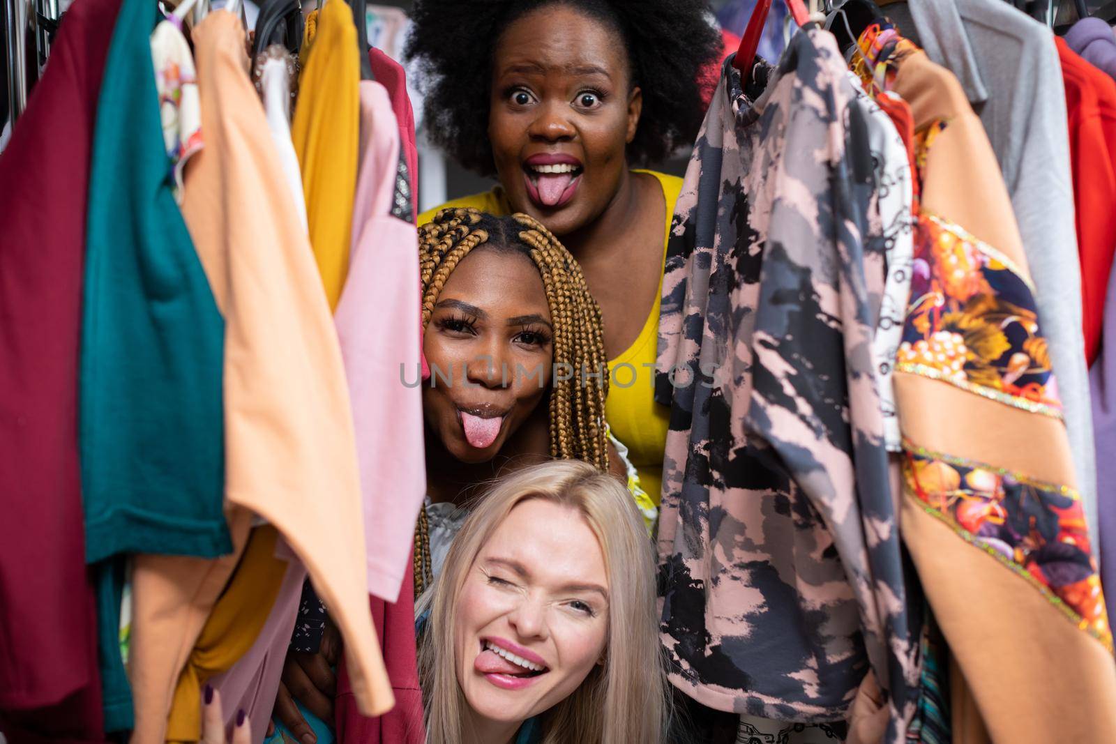 Three women stick out their tongues while standing one above the other. Madness and fun while shopping for the new summer season. Two African women and one European.