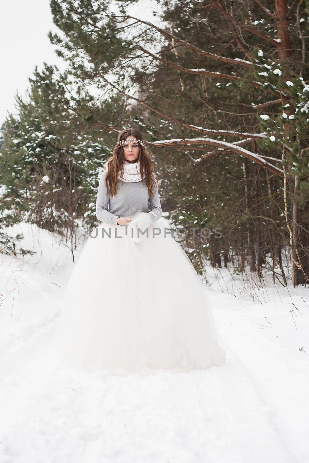 Beautiful bride in a white dress with a bouquet in a snow-covered winter forest. Portrait of the bride in nature.