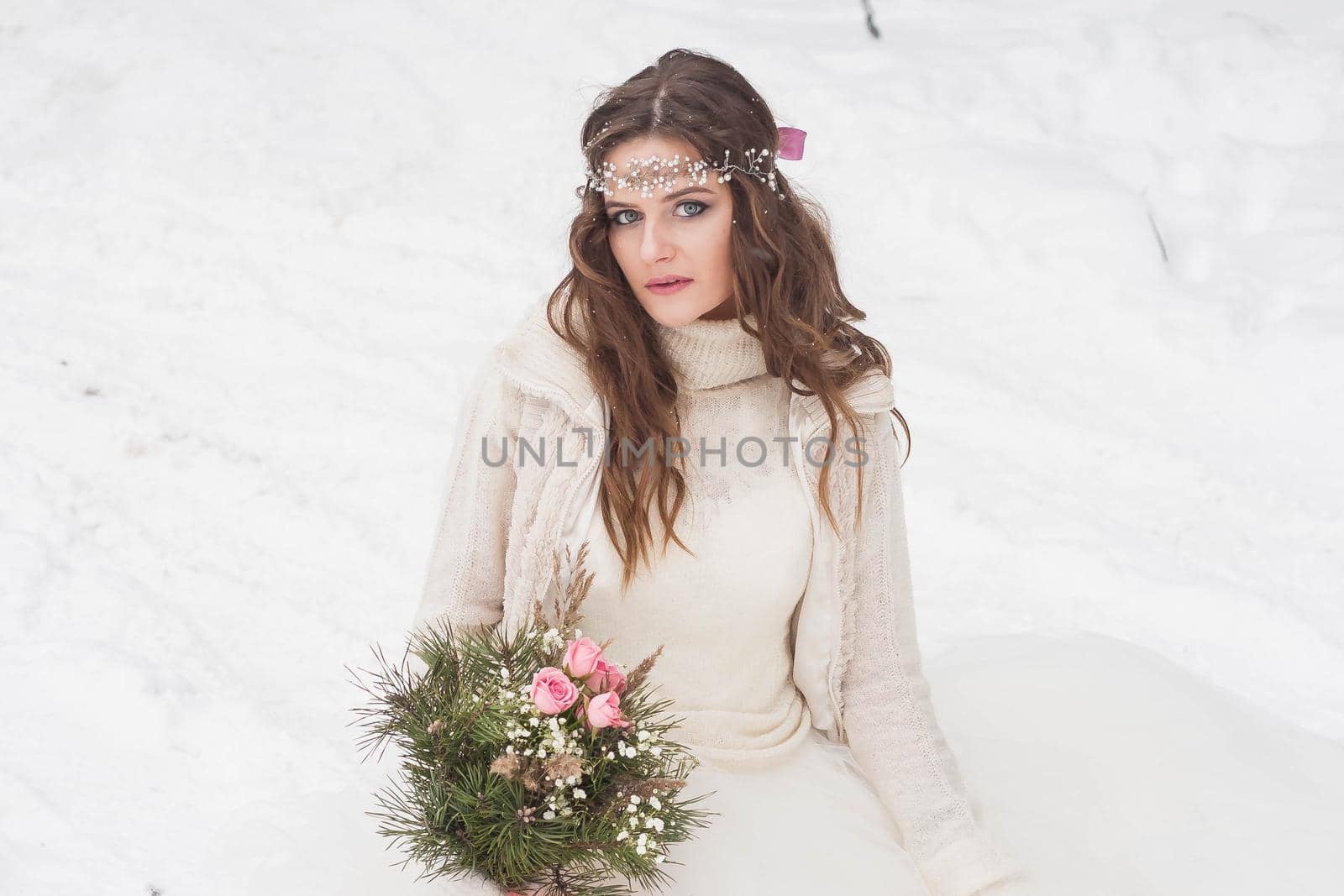 Beautiful bride in a white dress with a bouquet in a snow-covered winter forest. Portrait of the bride in nature.