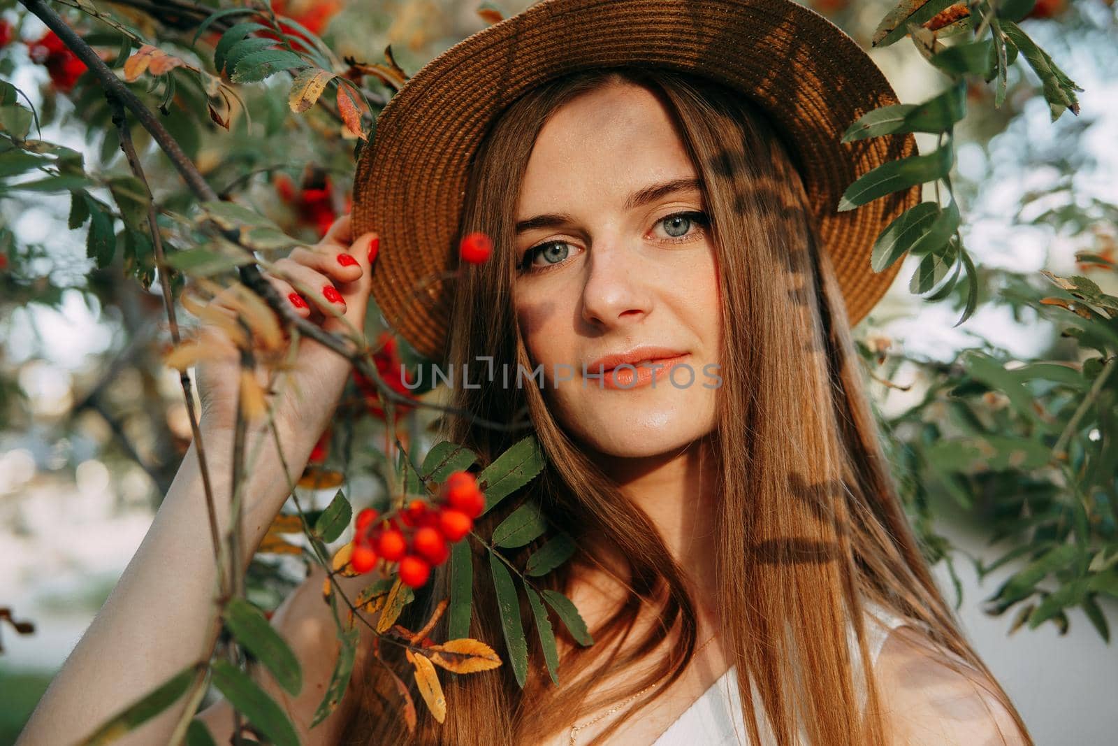 A beautiful blonde girl in a hat with long hair, on a walk in the autumn season. Portrait of a woman at a rowan tree by Annu1tochka