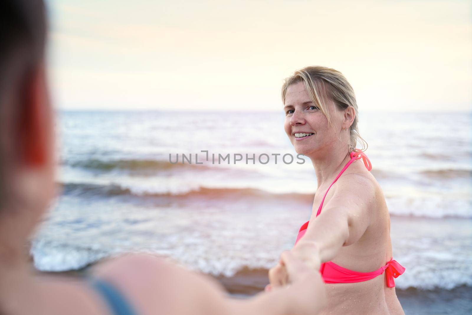follow me swimming. Smiling girl standing at sea and invites you to swim, follow me travel concept by PhotoTime