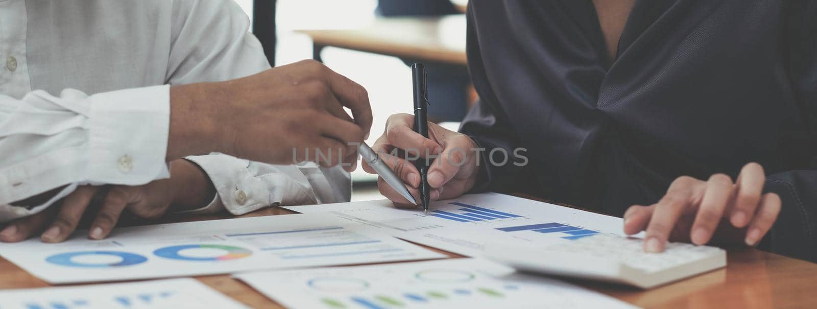 Cropped shot of business people hands holding pen and discussing about business plan, using computer and business graph, analyzing or calculating business results. by wichayada