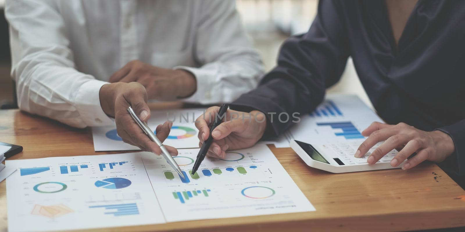 Cropped shot of business people hands holding pen and discussing about business plan, using computer and business graph, analyzing or calculating business results. by wichayada