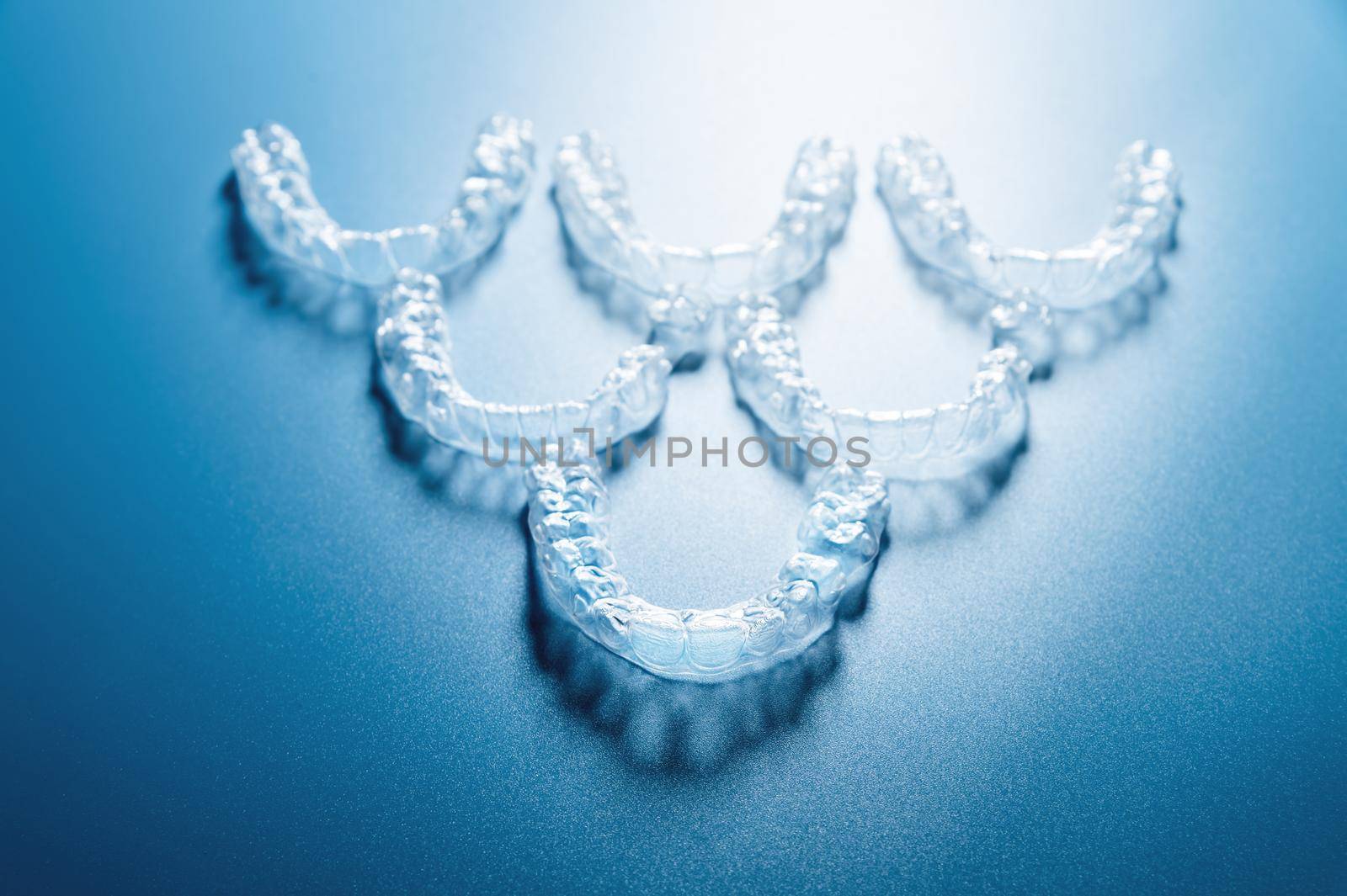 invisible plastic braces lie in reverse inverted pyramid shape in a row on a blue background, studio shot, nobody by yanik88