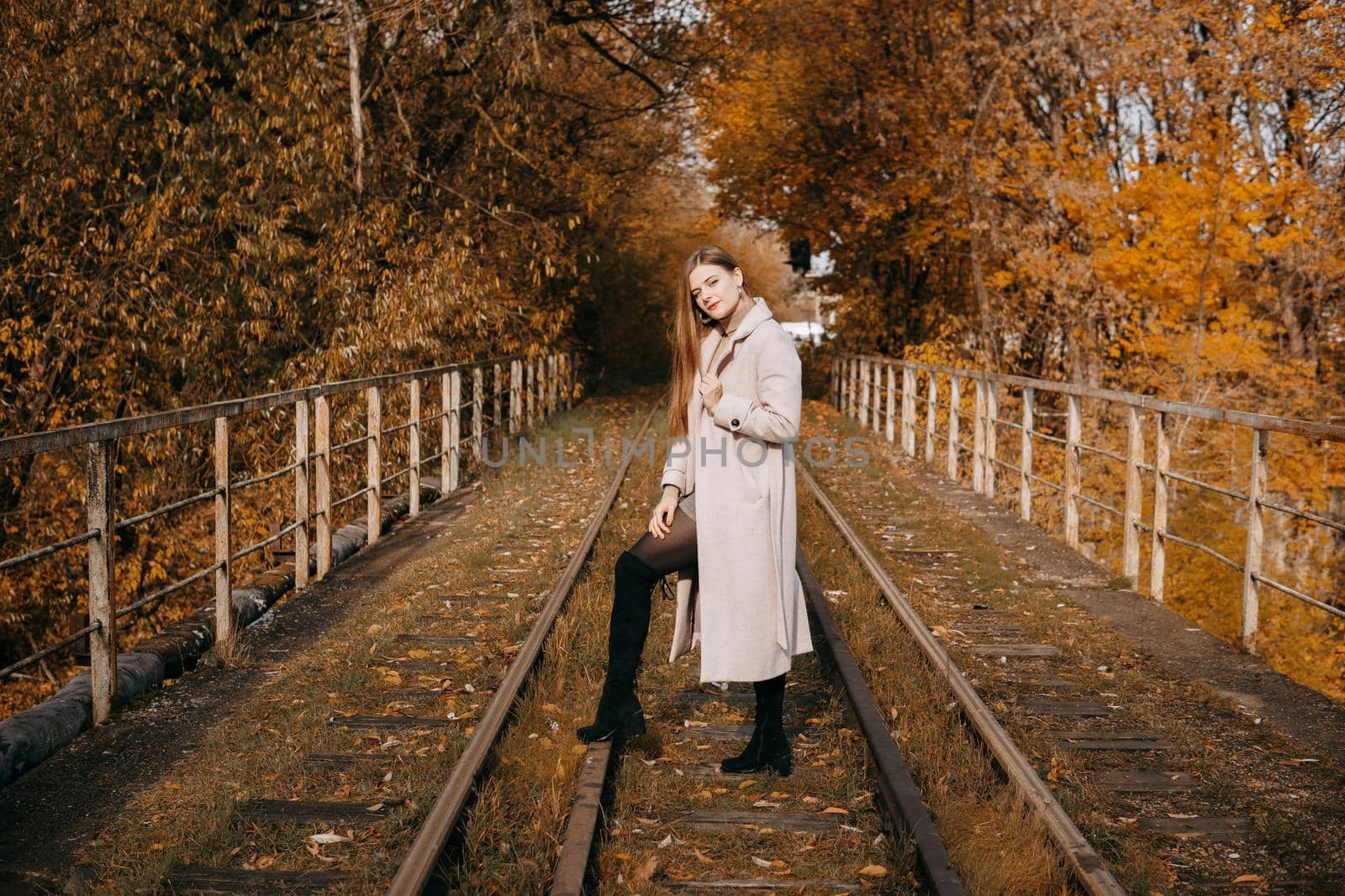 A beautiful long-haired woman walks through the autumn streets. Railway, autumn leaves, a woman in a light coat.