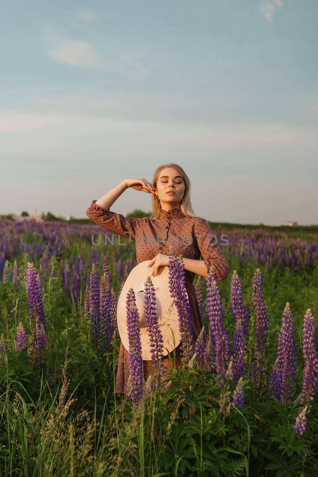 A beautiful woman in a straw hat walks in a field with purple flowers. A walk in nature in the lupin field.