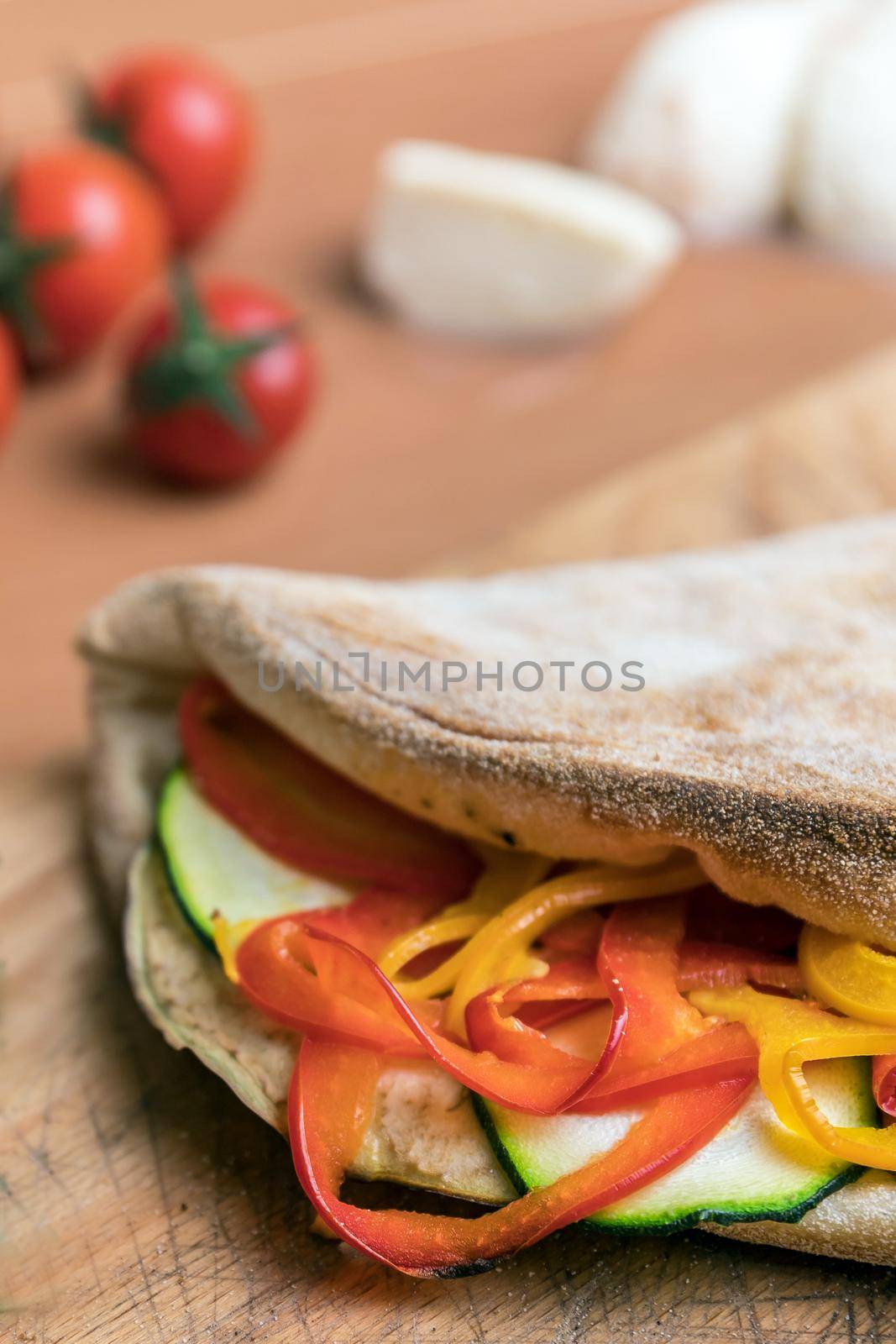 Italian food, closed calzone pizza on rustic wooden background. On background small red tomatoes, mozzarella and basil. Selective focus.