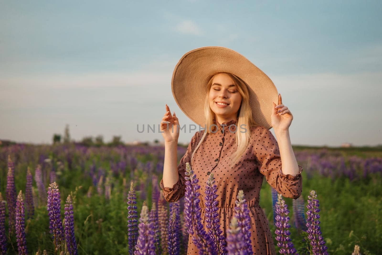 A beautiful woman in a straw hat walks in a field with purple flowers. A walk in nature in the lupin field.