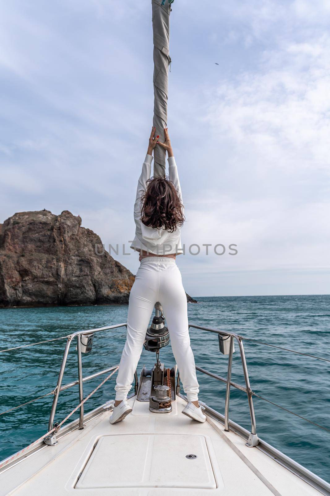 Woman standing on the nose of the yacht at a sunny summer day, breeze developing hair, beautiful sea on background by Matiunina