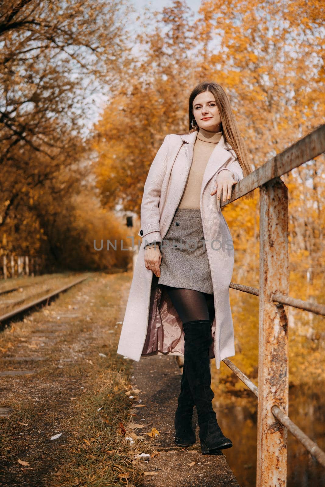 A beautiful long-haired woman walks through the autumn streets. Railway, autumn leaves, a woman in a light coat.