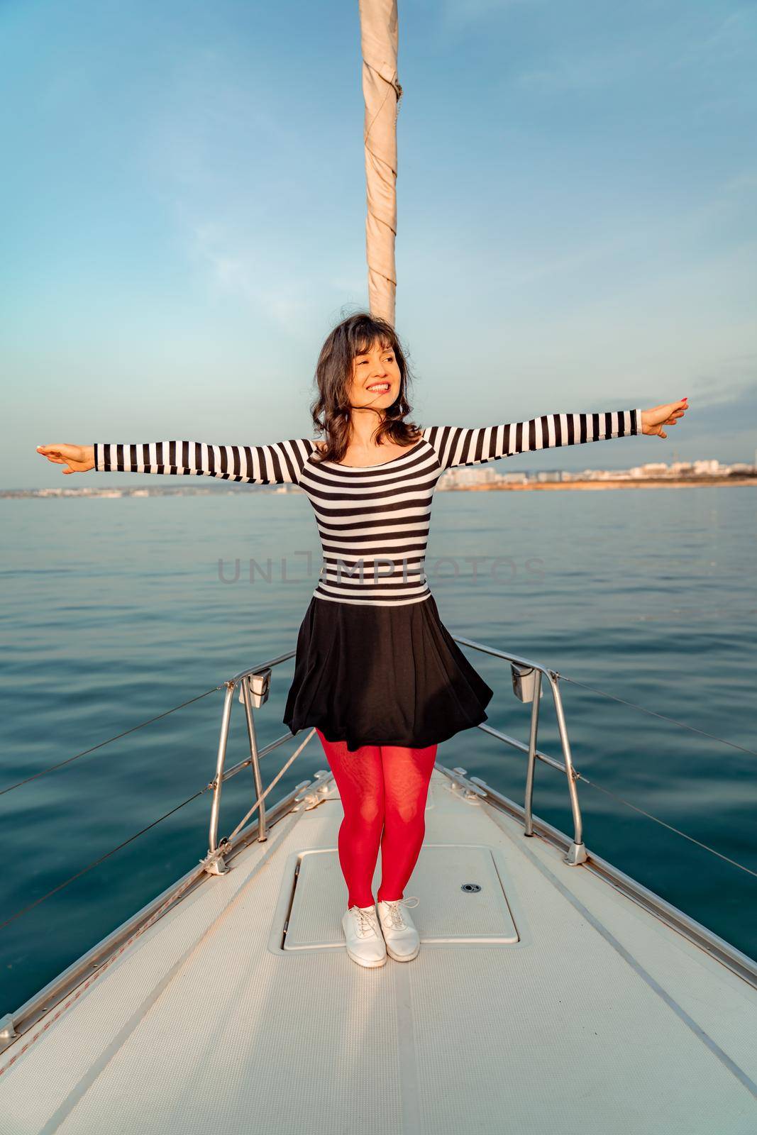 Woman standing on the nose of the yacht at a sunny summer day, breeze developing hair, beautiful sea on background.