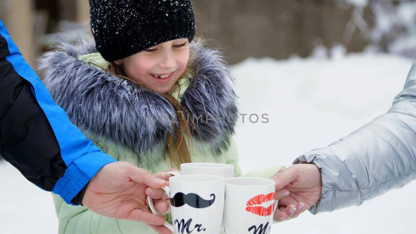 against the background of winter forest, a girl of seven years drinks tea from a cup, on the cups, sponges are drawn. Family tea in the winter forest, winter picnic. High quality photo