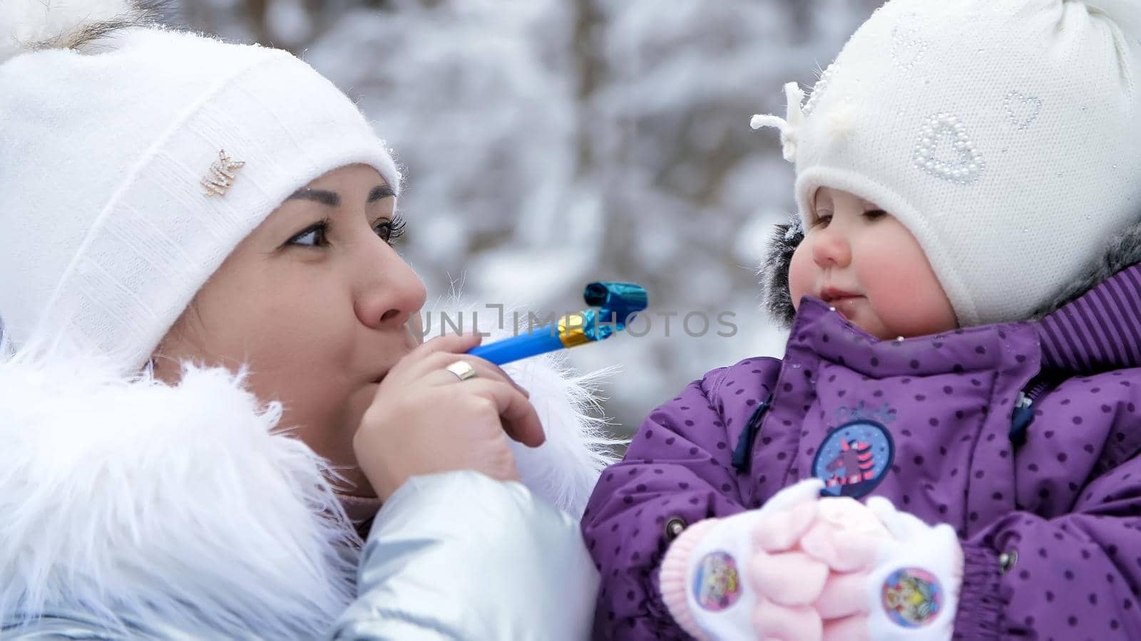 against the background of the winter forest, a young woman, Mom holds on her hands and amuses a one-year-old daughter . they are dressed in funny hats with bumbon. High quality photo