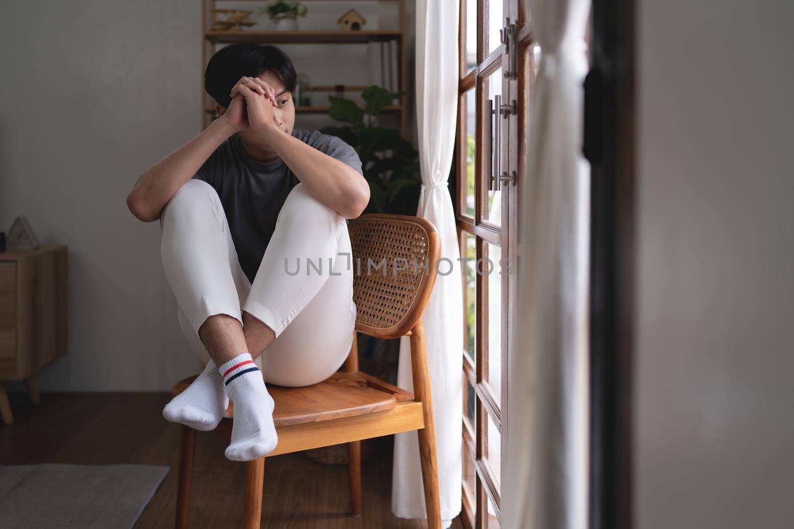 Portrait of worried guy sitting near window at home.