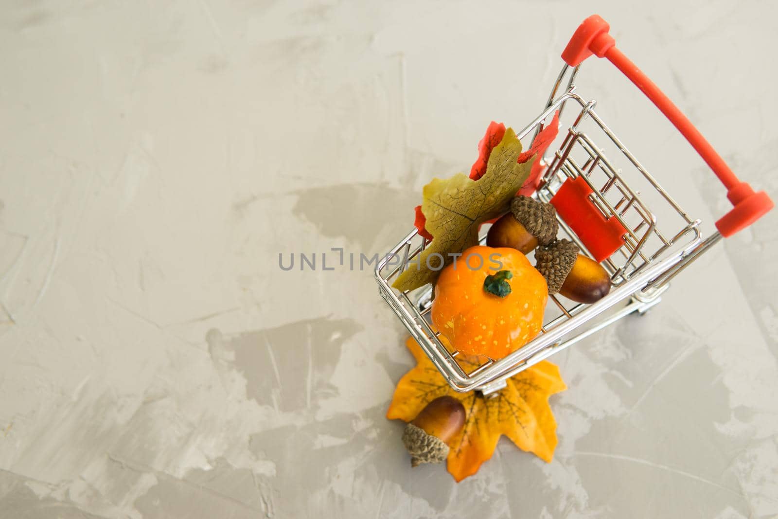 Grocery cart with decorative pumpkins and maple leaves on a concrete background. The concept of the autumn sales. Black Friday and cyber Monday. by Annu1tochka