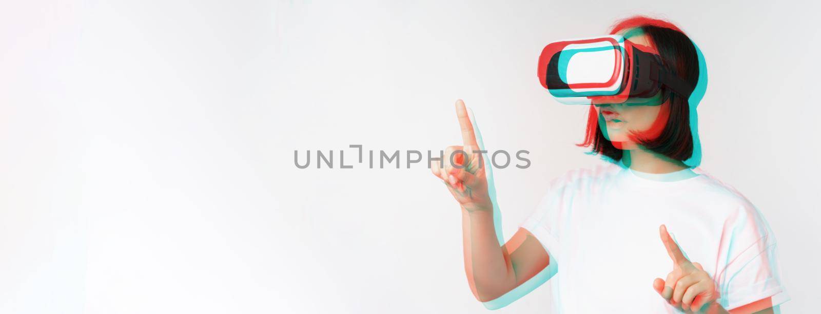 Potrait of asian woman in virtual reality glasses, pointing, choosing smth in VR headset, standing over white background.