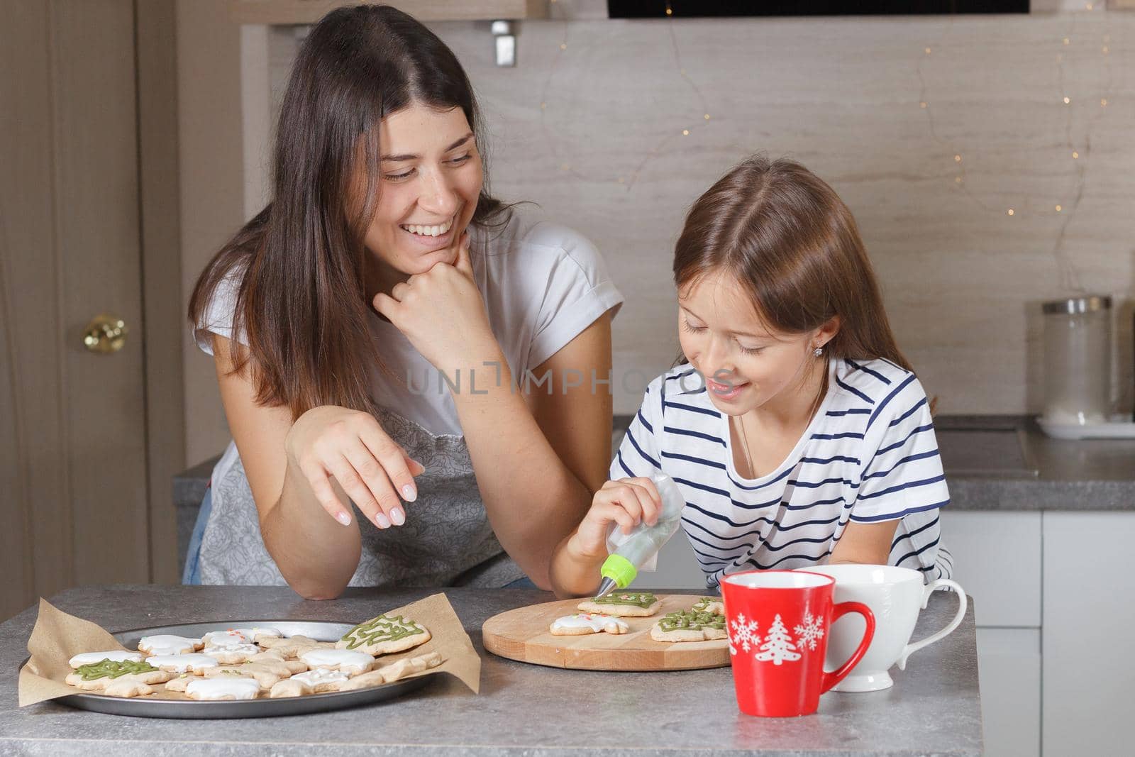 A little girl with her mother decorates Christmas cookies in the kitchen. Real life. by lara29