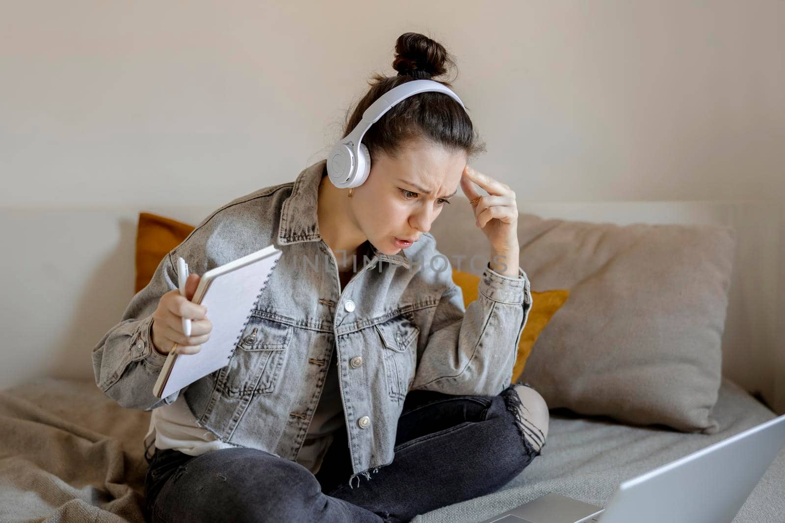 Angry and dissatisfied woman with casual clothes sitting on bed at home with computer and studying. Girl is sad and tired. Negative emotions, stress, mental problems, deadline. Distance education