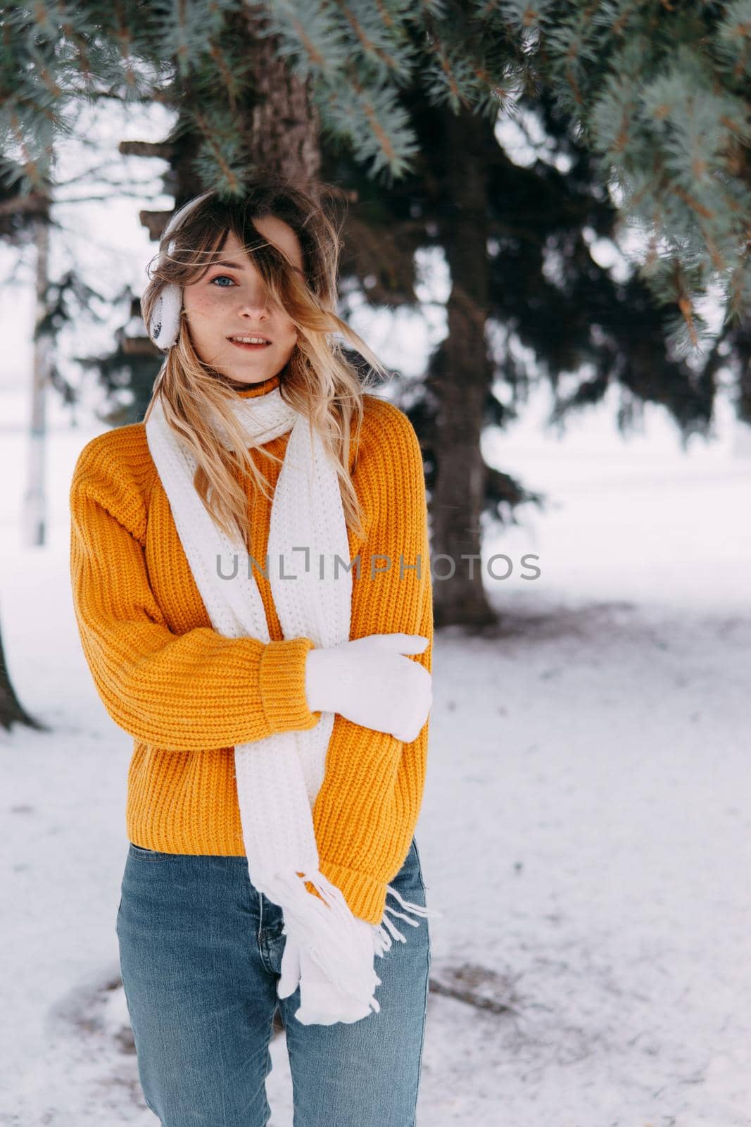 Teen blonde in a yellow sweater outside in winter. A teenage girl on a walk in winter clothes in a snowy forest.