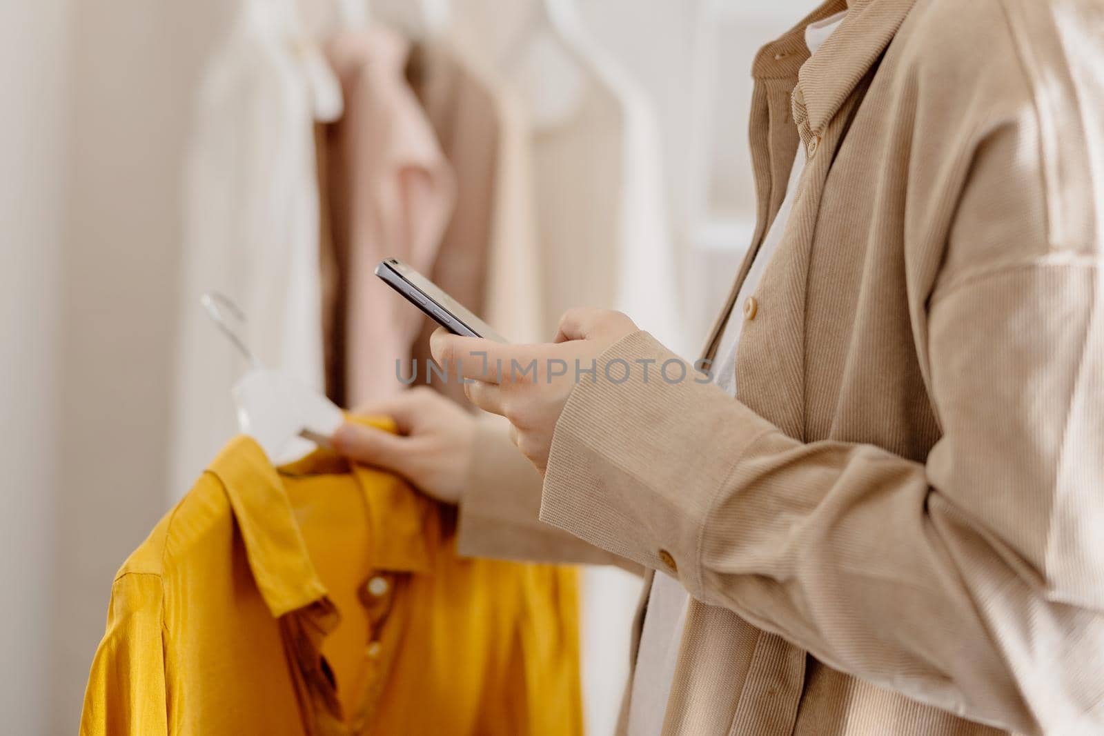 Woman holding smartphone and taking photo of her old clothes to sell them online. Selling on website, e-commerce. Reuse, second-hand concept. Conscious consumer, sustainable lifestyle. Close-up view