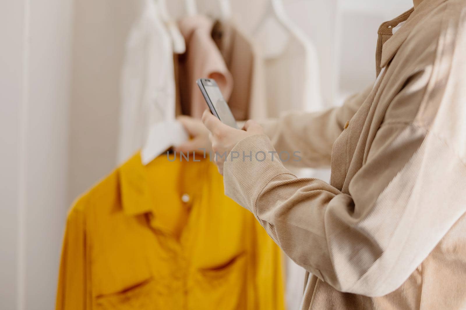 Woman holding smartphone and taking photo of her old clothes to sell them online. Selling on website, e-commerce. Reuse, second-hand concept. Conscious consumer, sustainable lifestyle. Close-up view