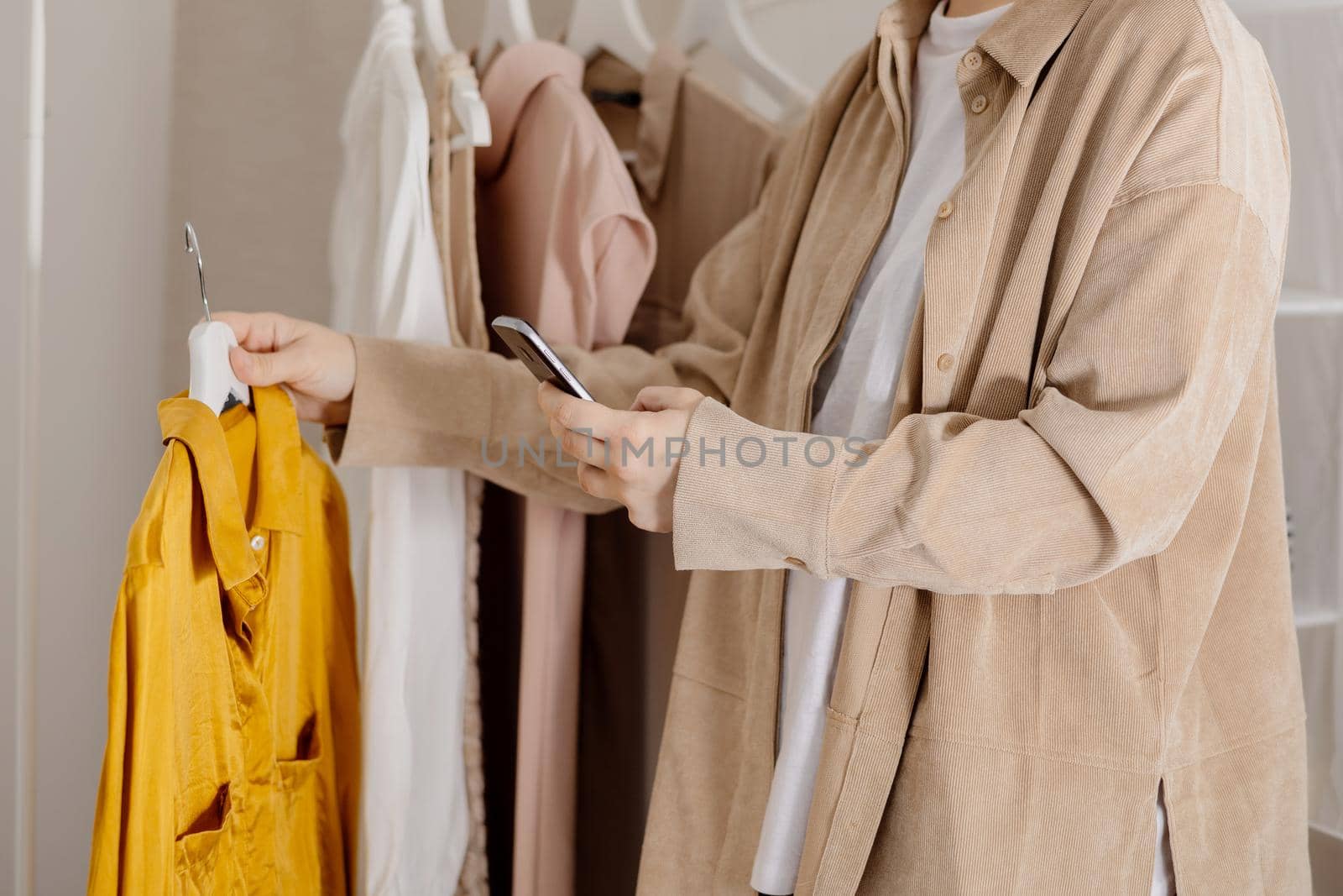 Woman holding smartphone and taking photo of her old clothes to sell them online. Selling on website, e-commerce. Reuse, second-hand concept. Conscious consumer, sustainable lifestyle. Close-up view