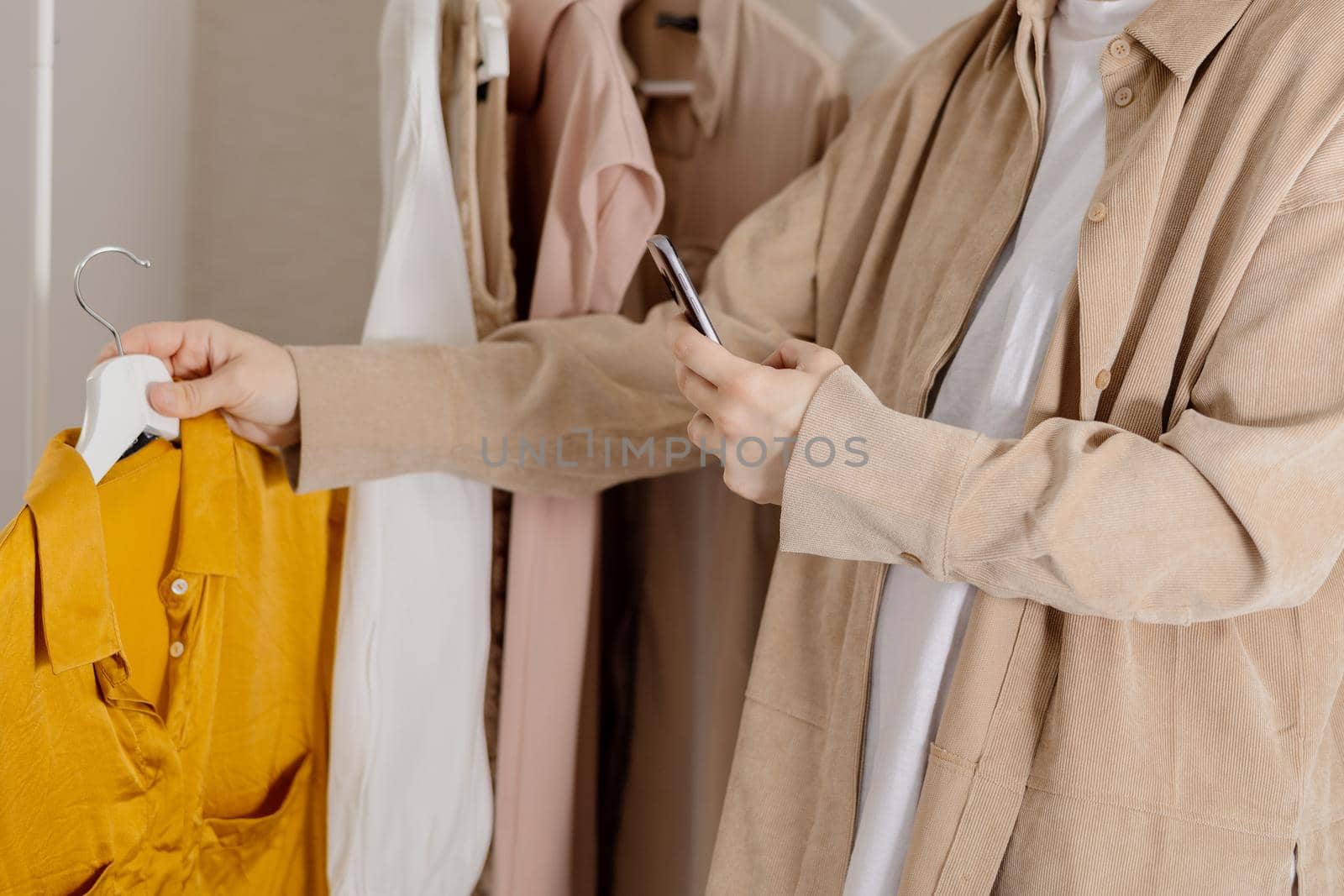 Woman holding smartphone and taking photo of her old clothes to sell them online. Selling on website, e-commerce. Reuse, second-hand concept. Conscious consumer, sustainable lifestyle. Close-up view