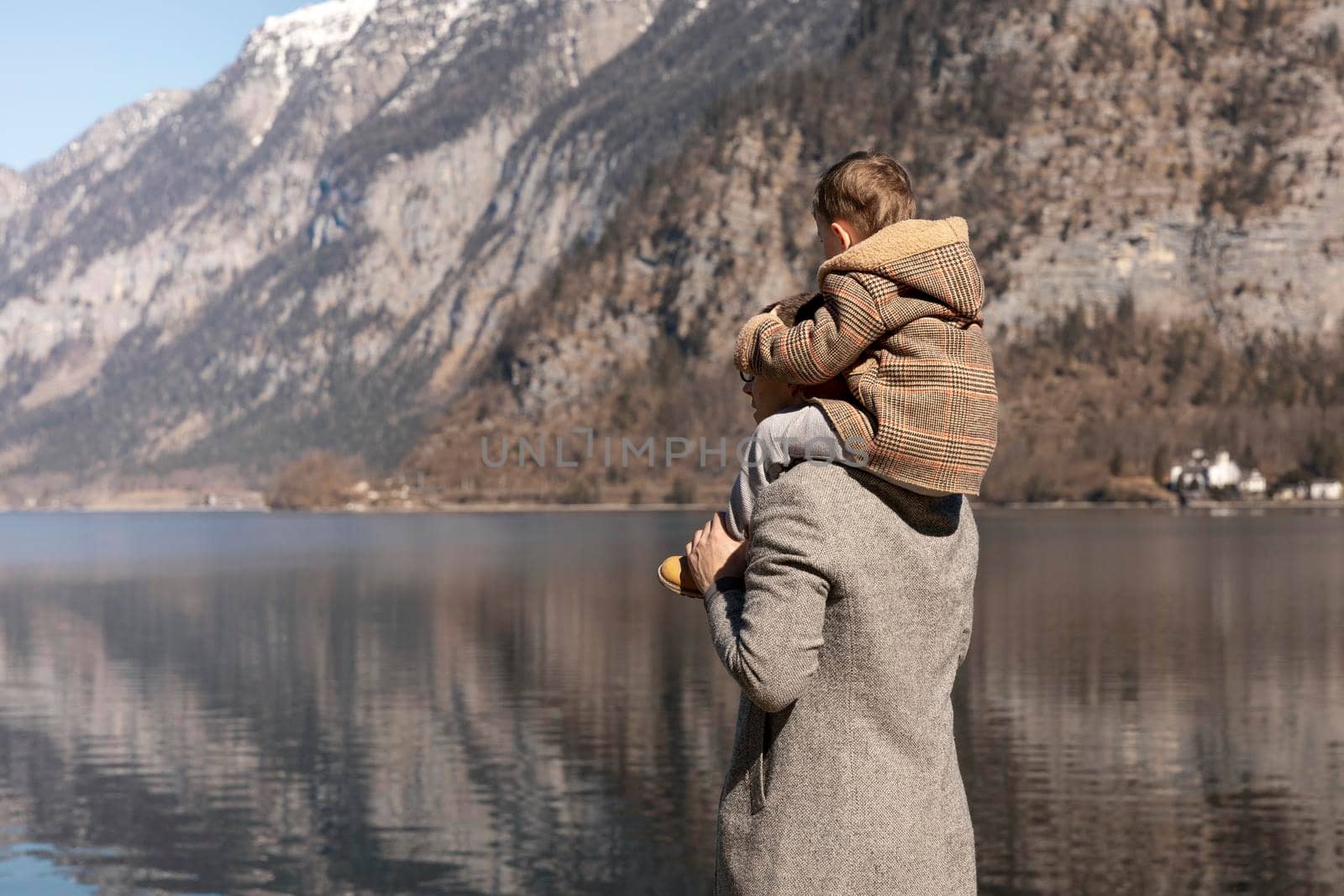 Father and son enjoying mountains, snow, lake, good weather, blue sky, sun. Little boy and his father spending time together. Family time. Beautiful landscape. Tourism, holiday, travel. Amazing view