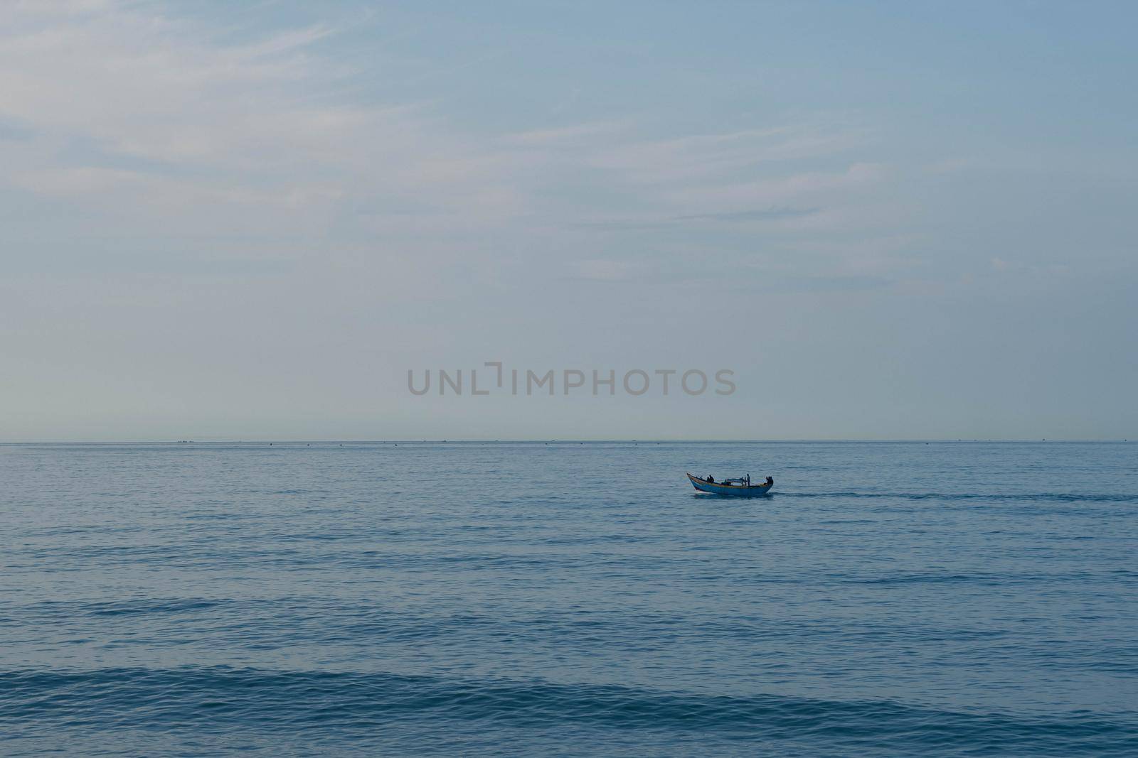 Simple background Calm dark blue sea fishing boat alone white pale Spindrift clouds Open way no limitations.
