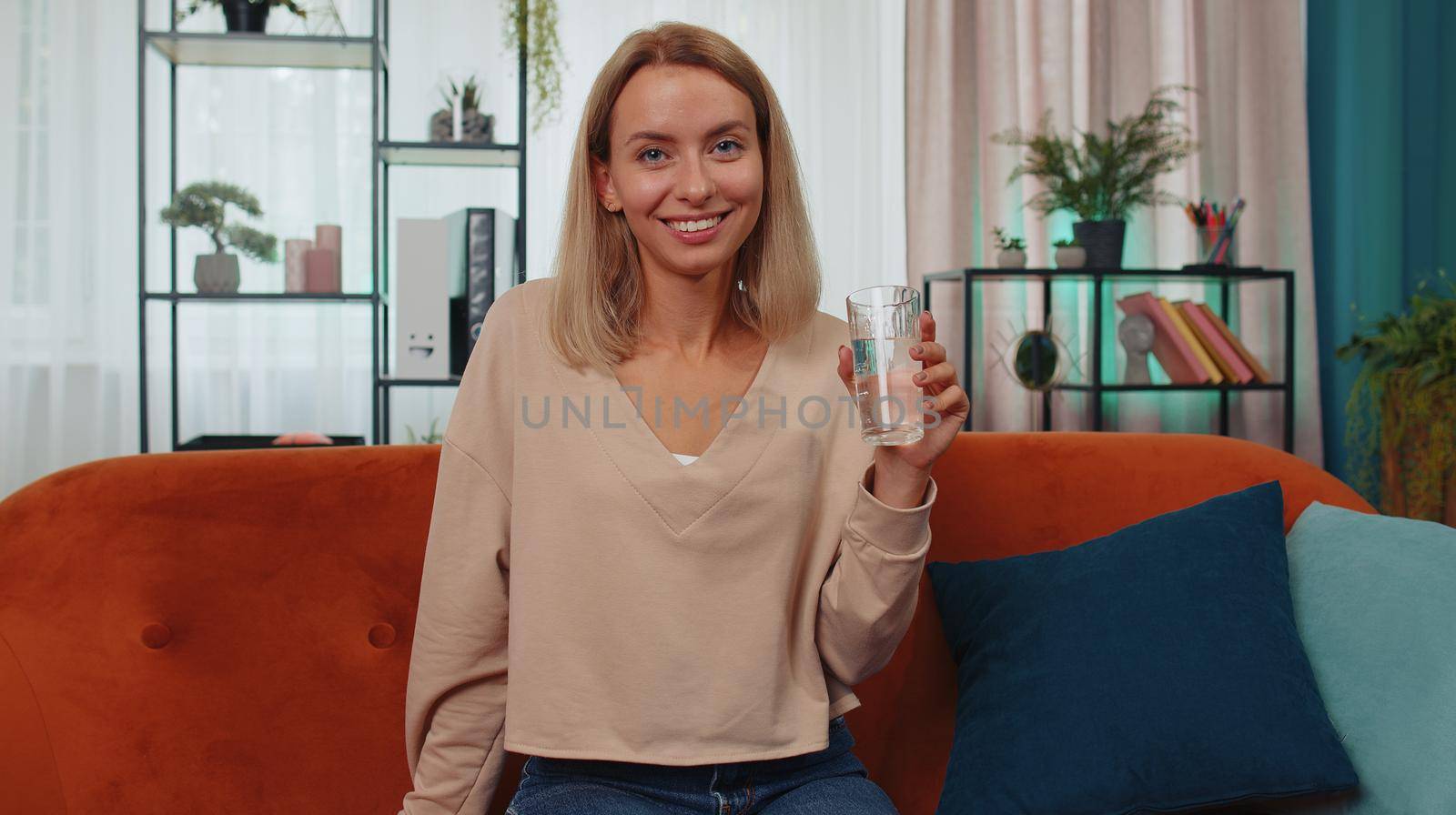 Portrait of thirsty lovely girl sitting indoors holding glass of natural aqua make sips drinking still water preventing dehydration. Woman with good life habits, healthy slimming, weight loss concept