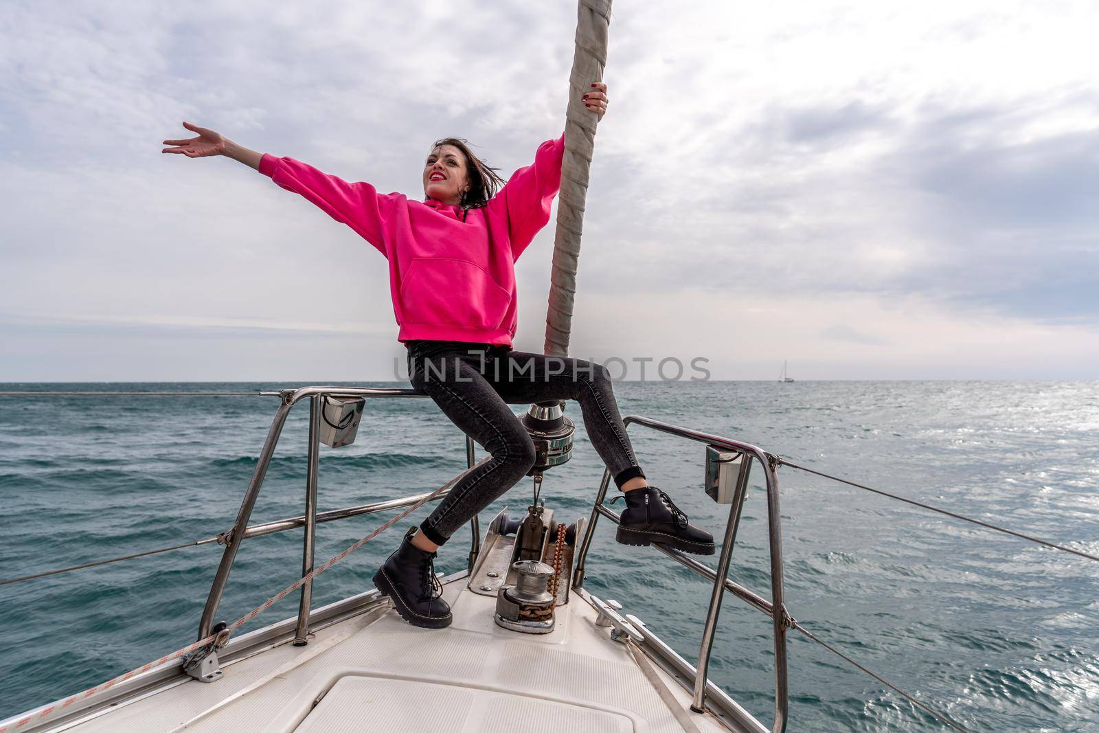 Woman standing on the nose of the yacht at a sunny summer day, breeze developing hair, beautiful sea on background.