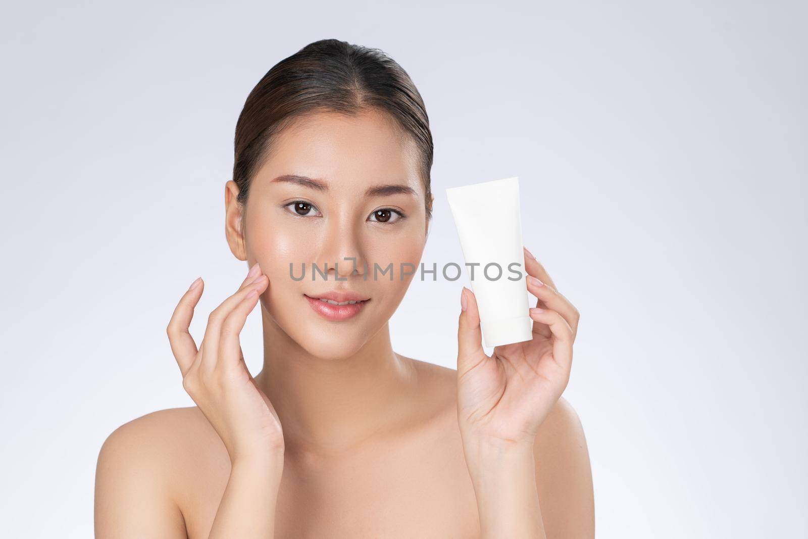 Gorgeous woman smiling holding mockup product for advertising text place, light grey background. Concept of healthcare for skin, beauty care product for advertising.