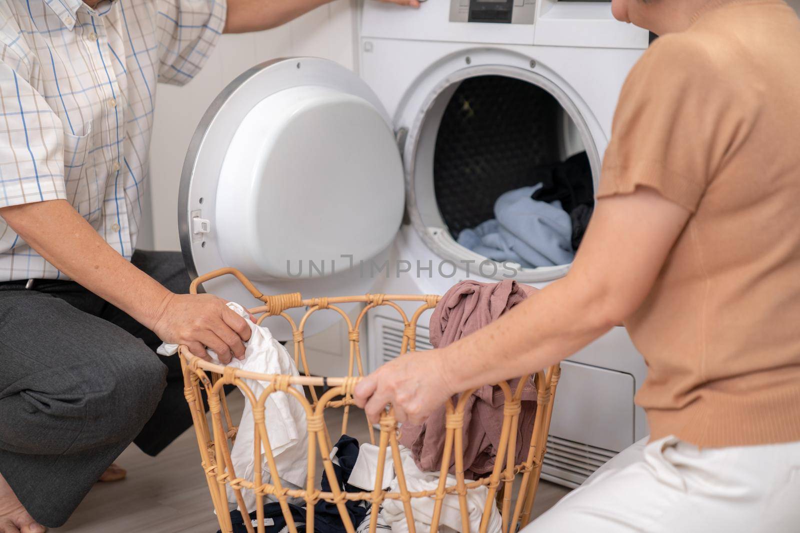 Senior couple working together to complete their household chores at the washing machine in a happy and contented manner. Husband and wife doing the usual tasks in the house.