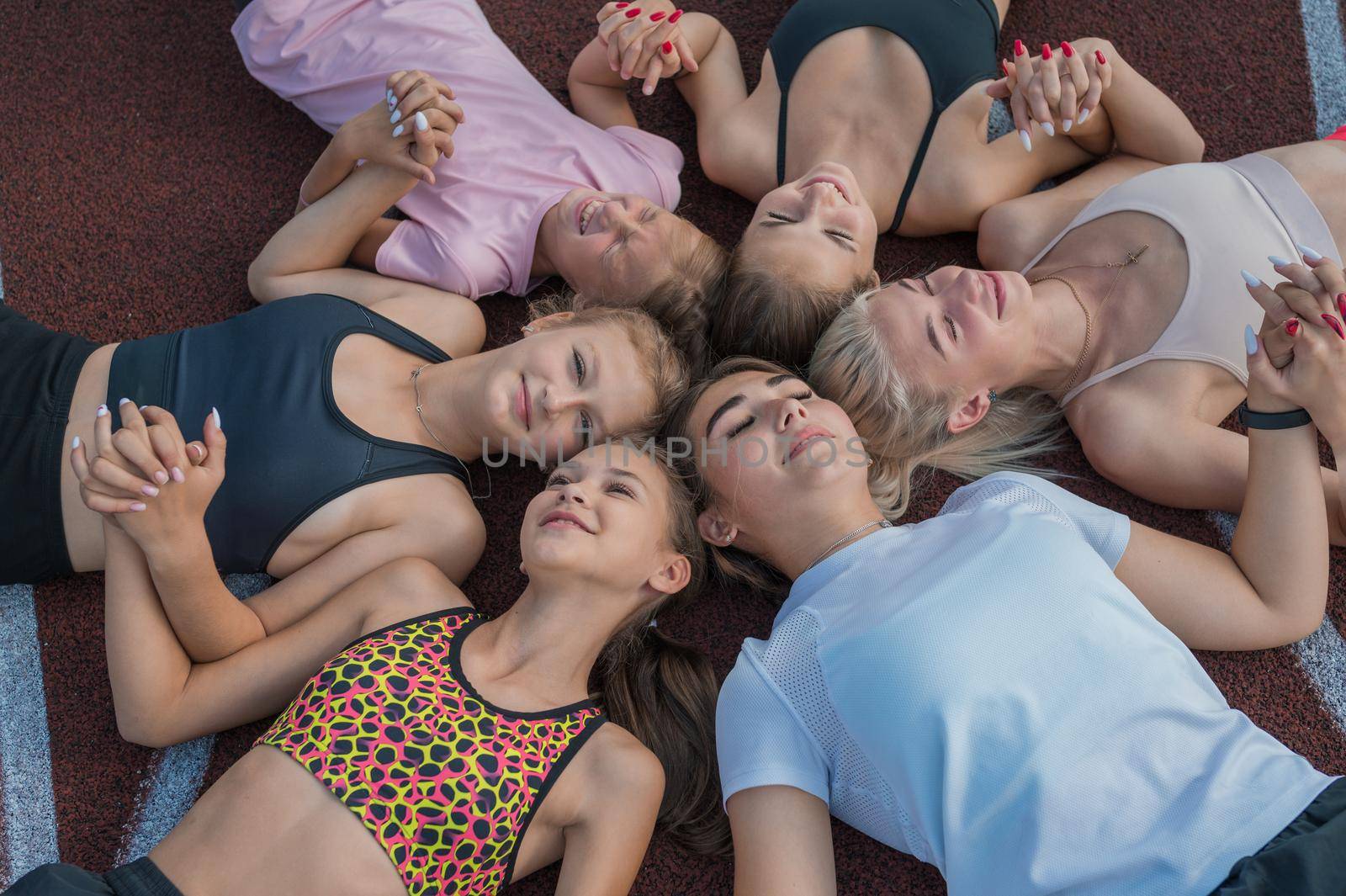 Group of tired and happy fit young girls resting on floor at stadium