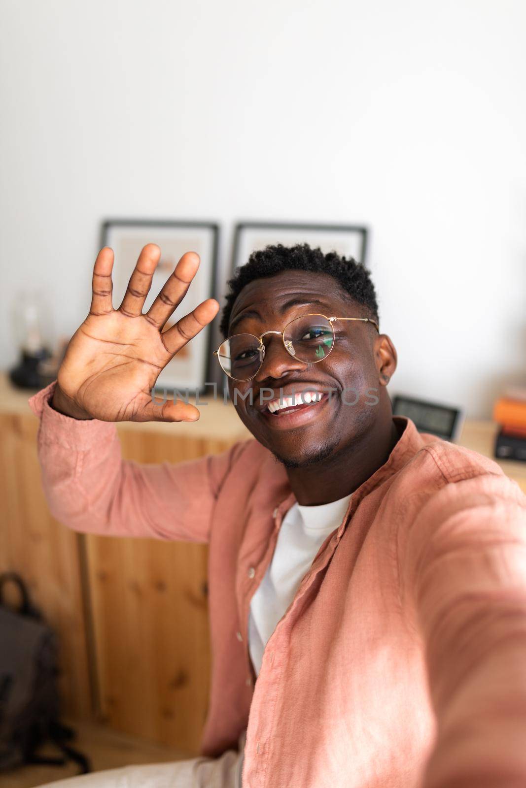 Black young man looking at camera waving hello during video call using phone. Man taking selfie at home. Copy space. Vertical image. Social media and technology concept.