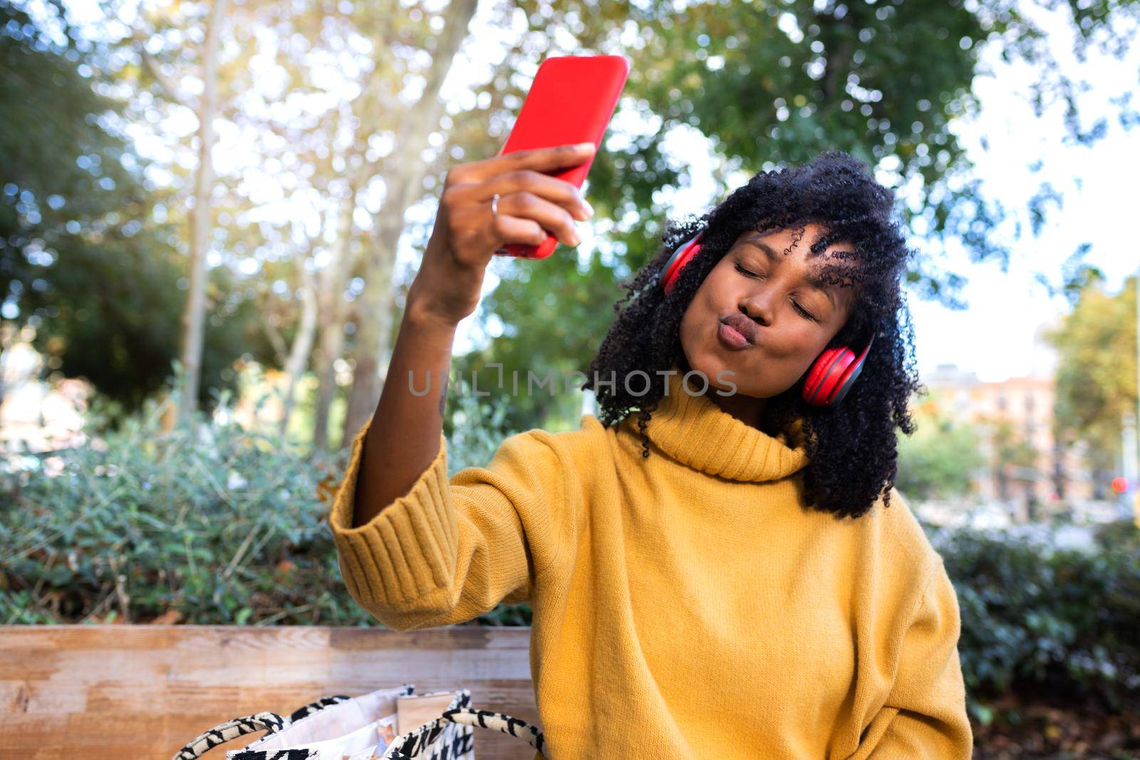 Young African American woman taking a selfie pouting sending kisses in public park. Copy space. Lifestyle and technology concept.