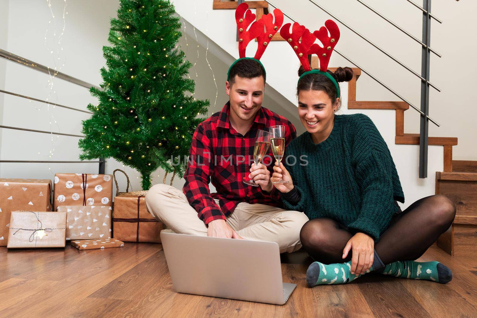 Young caucasian couple celebrate Christmas with family toasting with champagne on video call. Holiday concept.