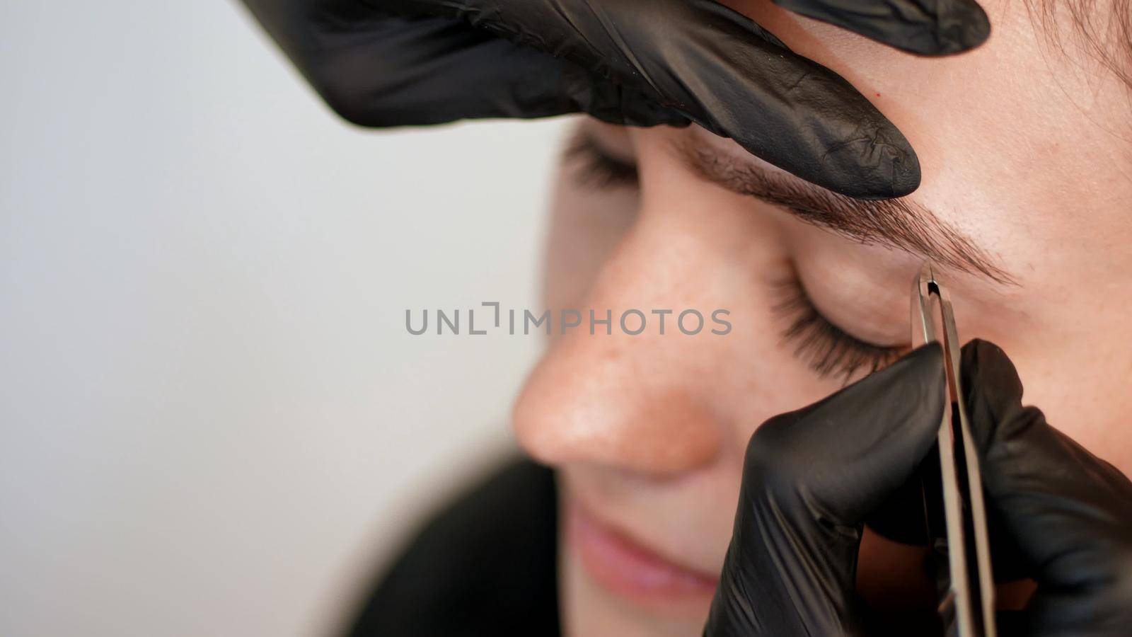 beauty saloon. close-up, hands of the cosmetician in black rubber gloves hold tweezers and pull out eyebrows. Master corrects the shape of the eyebrows. High quality photo