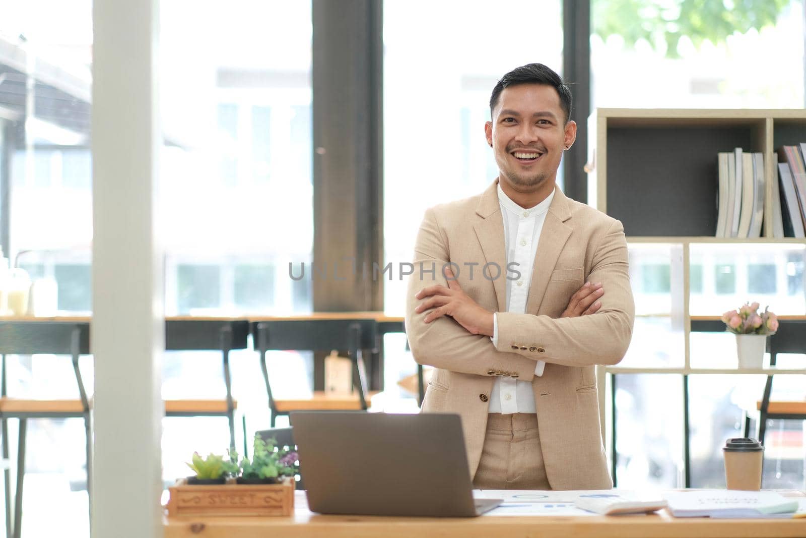 Asian businessman standing by his desk in office by wichayada