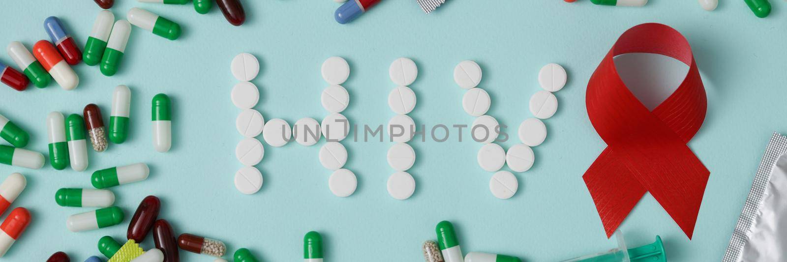 The word HIV is written with pills, condoms and capsules on a blue background, close-up. Aids protection concept