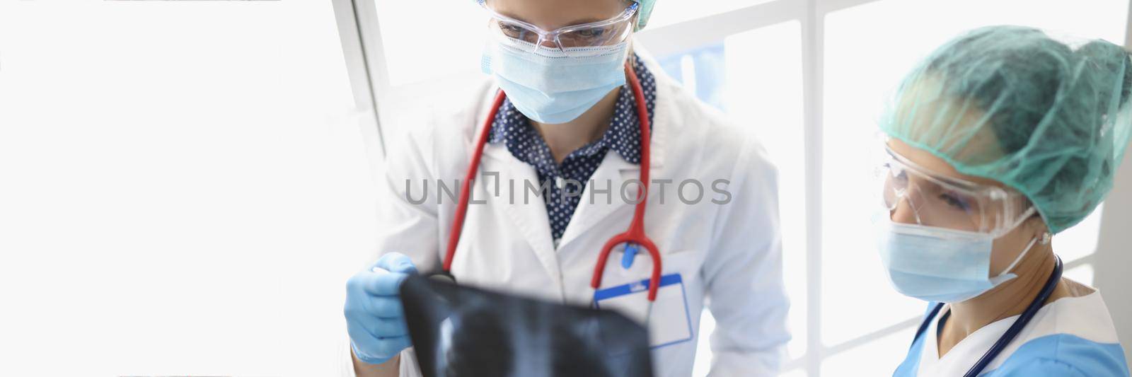 Two female doctors in the clinic are looking at an x-ray of the lungs, close-up. Diagnosis of pneumonia, viral disease, omicron