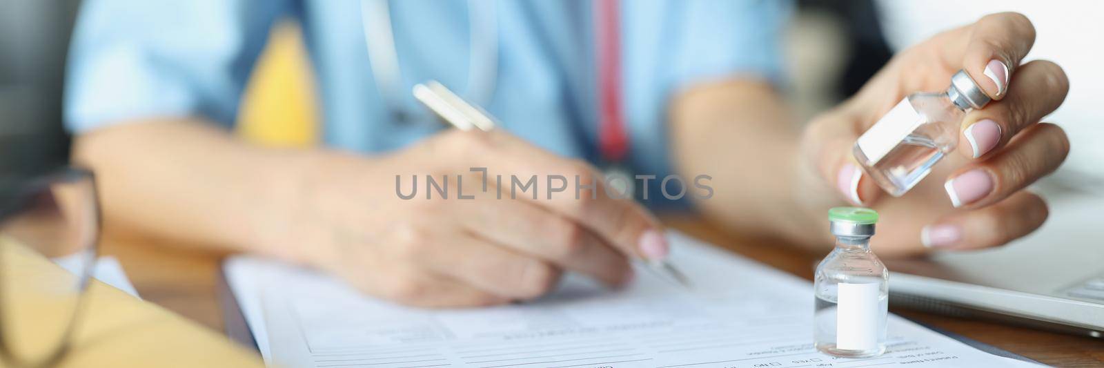 A female doctor holds a vaccine and writes a prescription, hand close-up, blurry. Selection of medicines for treatment