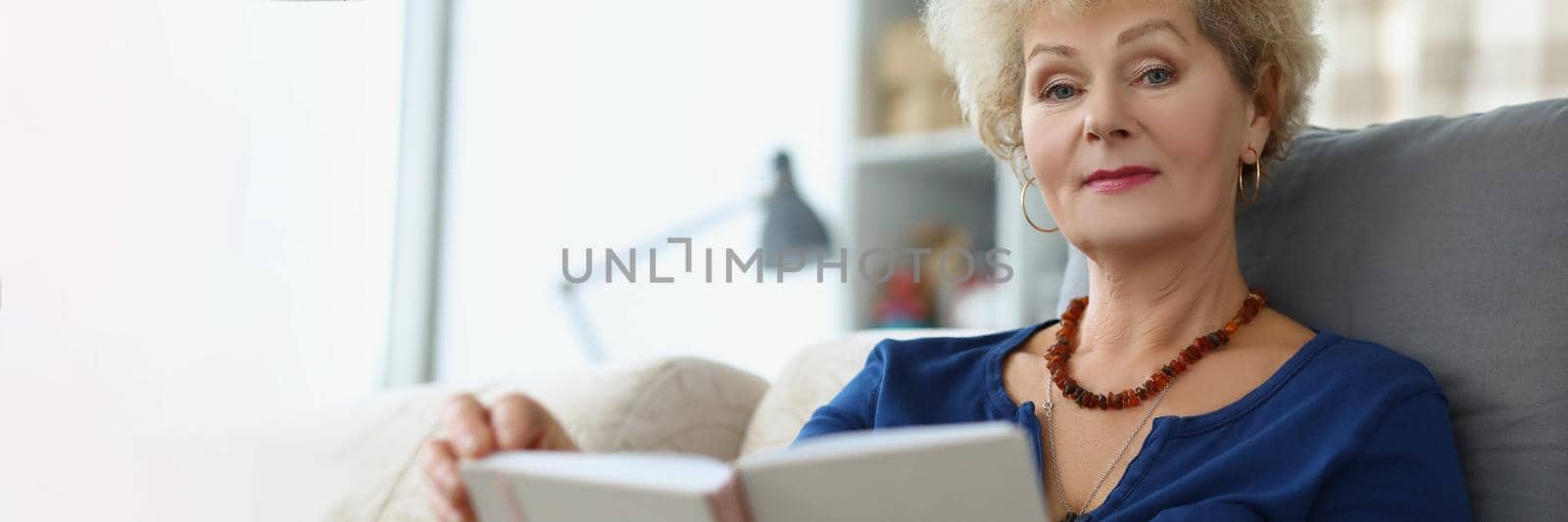 An elderly woman reads a book at home by kuprevich