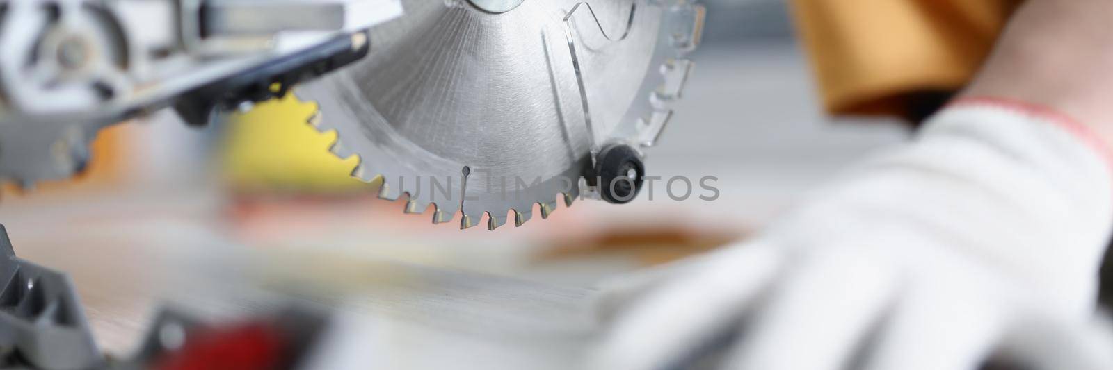 Male hands in gloves next to a circular saw, close-up, blurry. Woodworking workshop, sawing boards, carpenter equipment