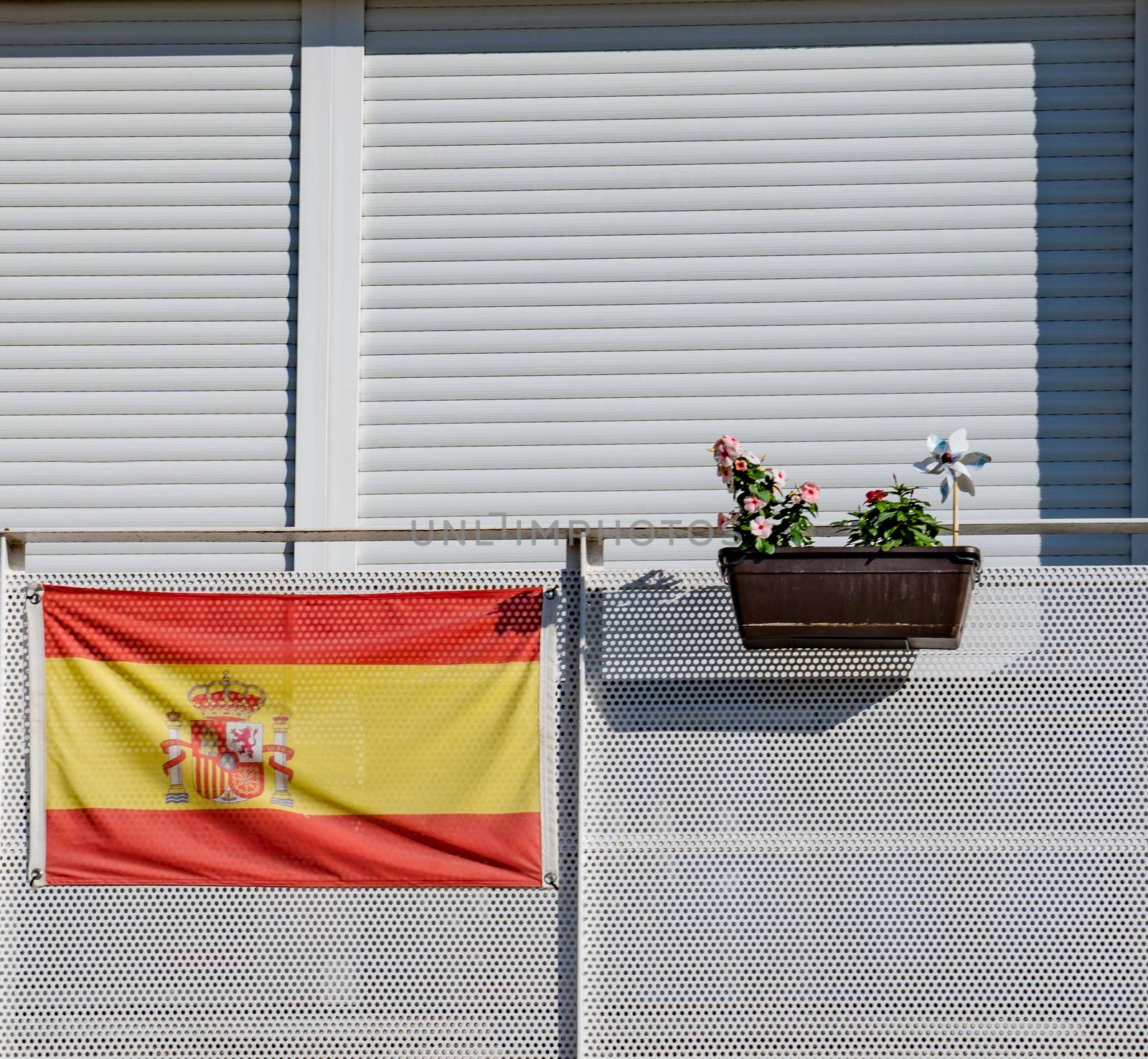 Spanish flag on a white color balcony and a plot with flowers.