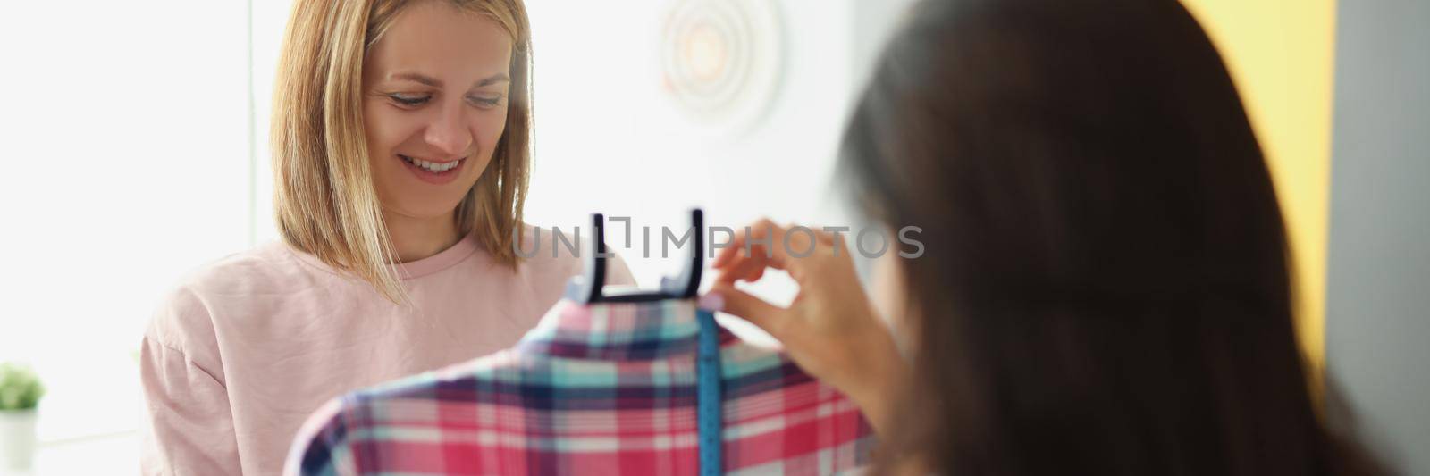 A woman seamstress shows a client a blouse in close-up, blurry. Sewing atelier, clothing designer, dressmaker