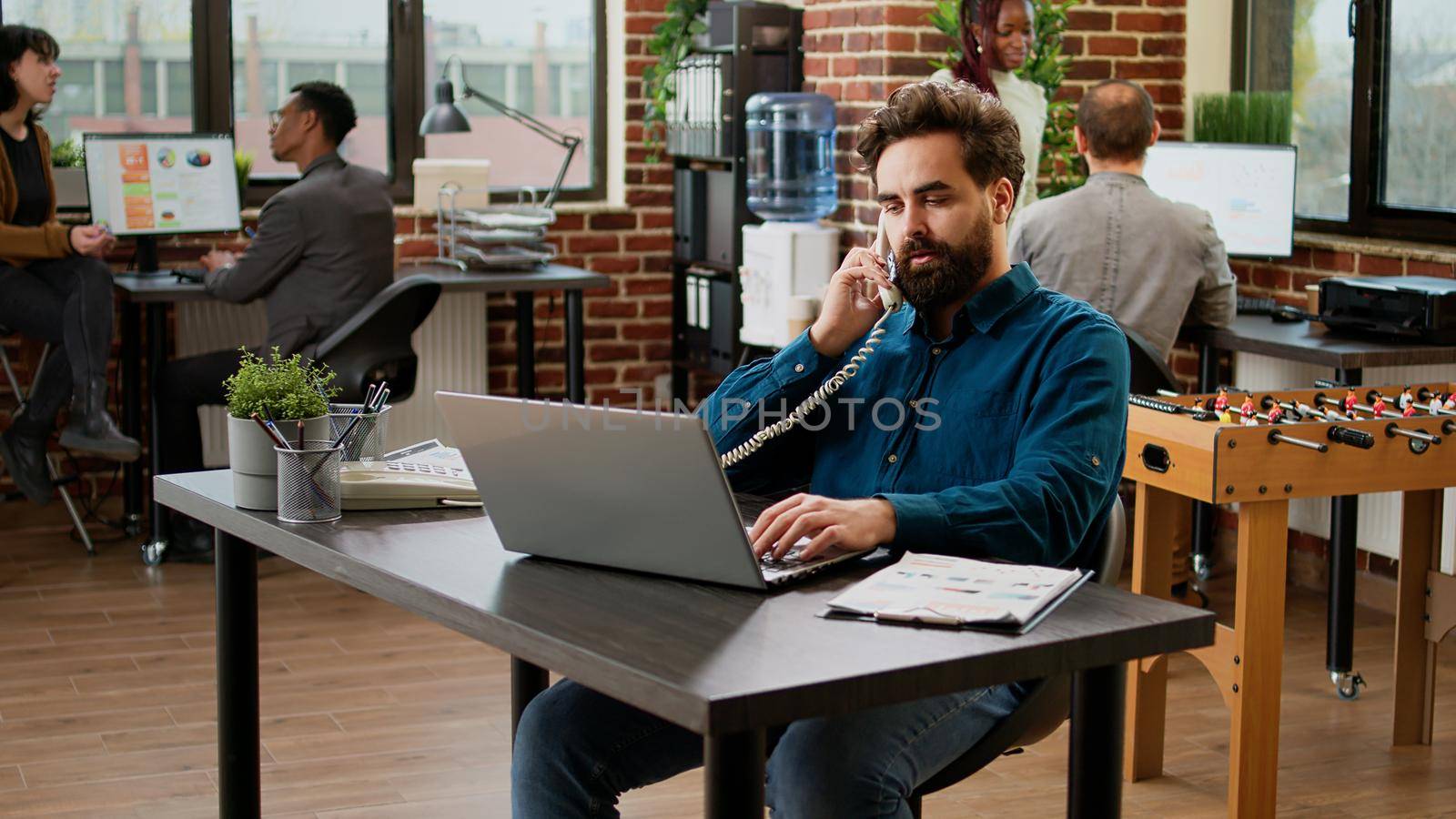 Project manager answering landline phone call in startup office, talking to employee on phone line. Using office telephone with cord to chat and have remote communication at job.
